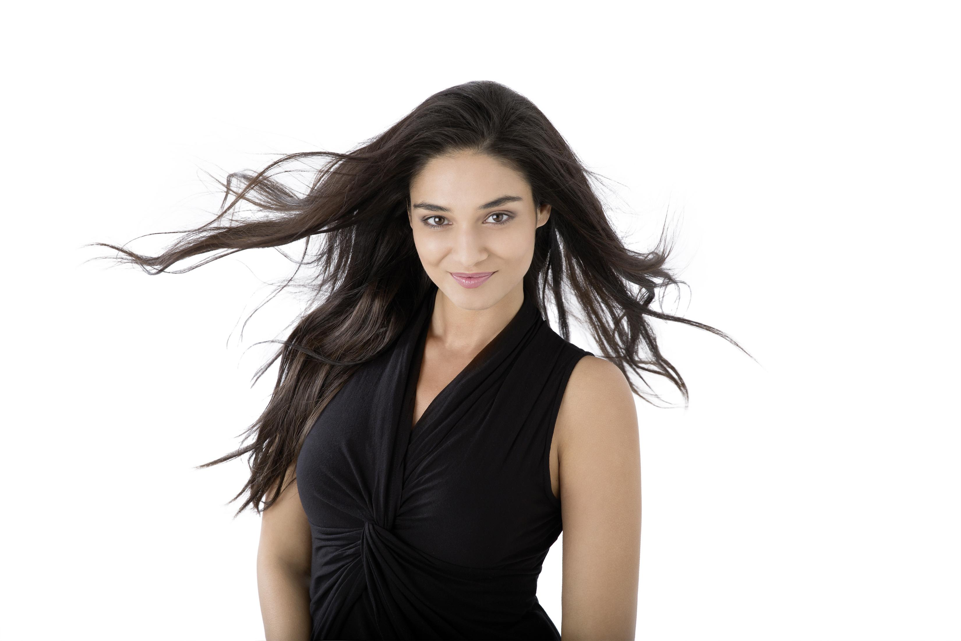 Eine Frau mit langen, dunklen Haaren in einem schwarzen Kleid vor weißem Hintergrund.