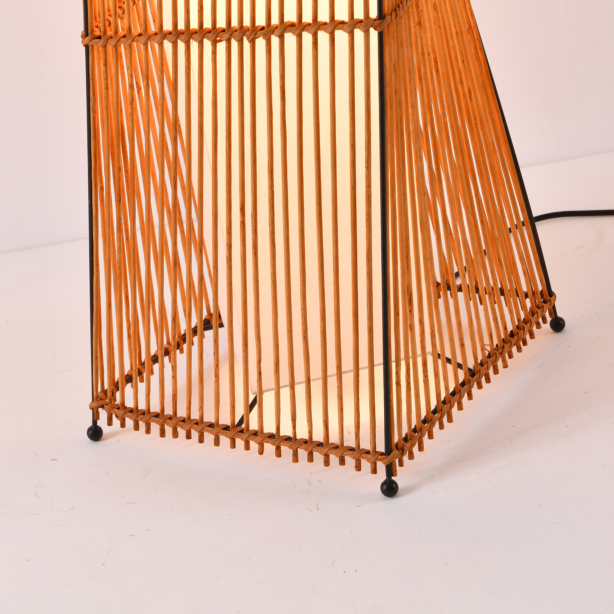 Eine gewebte Bambuslampe mit einer inneren Lichtquelle, vor weißem Hintergrund.