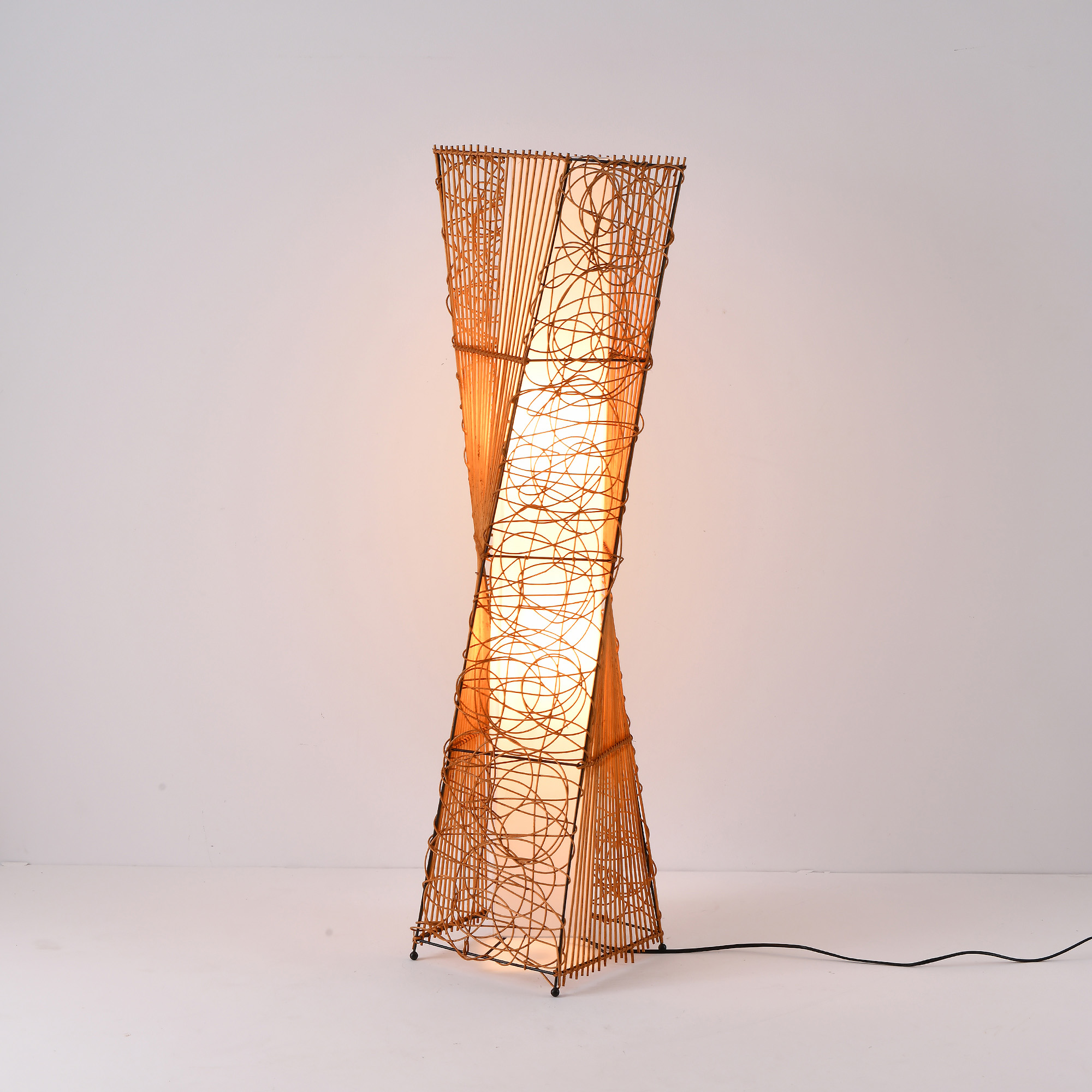 Hohe, beleuchtete, gewebte Lampe mit Spiraldesign. Braune Farbe, Licht scheint durch die Struktur.