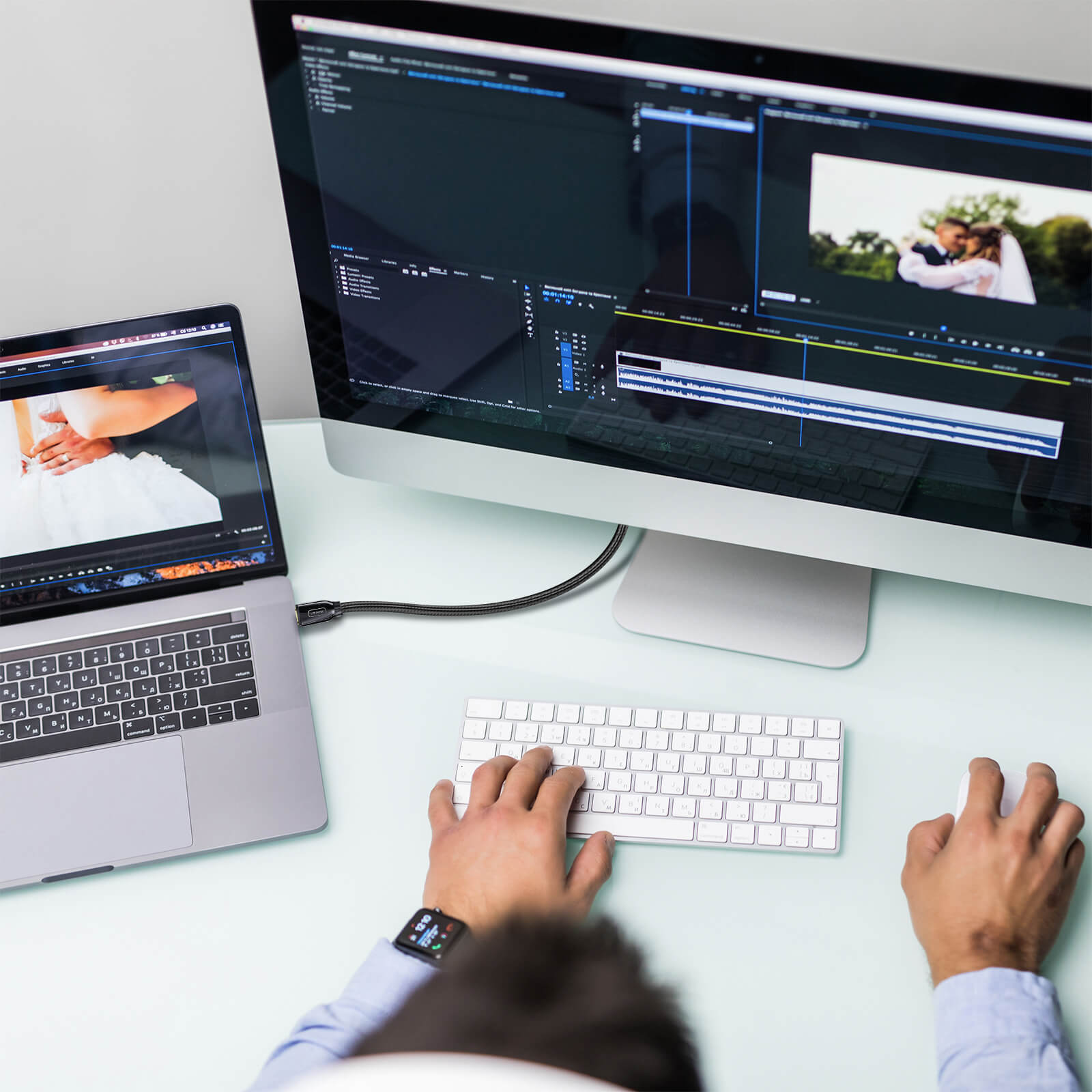 Person bearbeitet Video auf Laptop und großem Monitor, Tastatur und Maus auf dem Tisch.