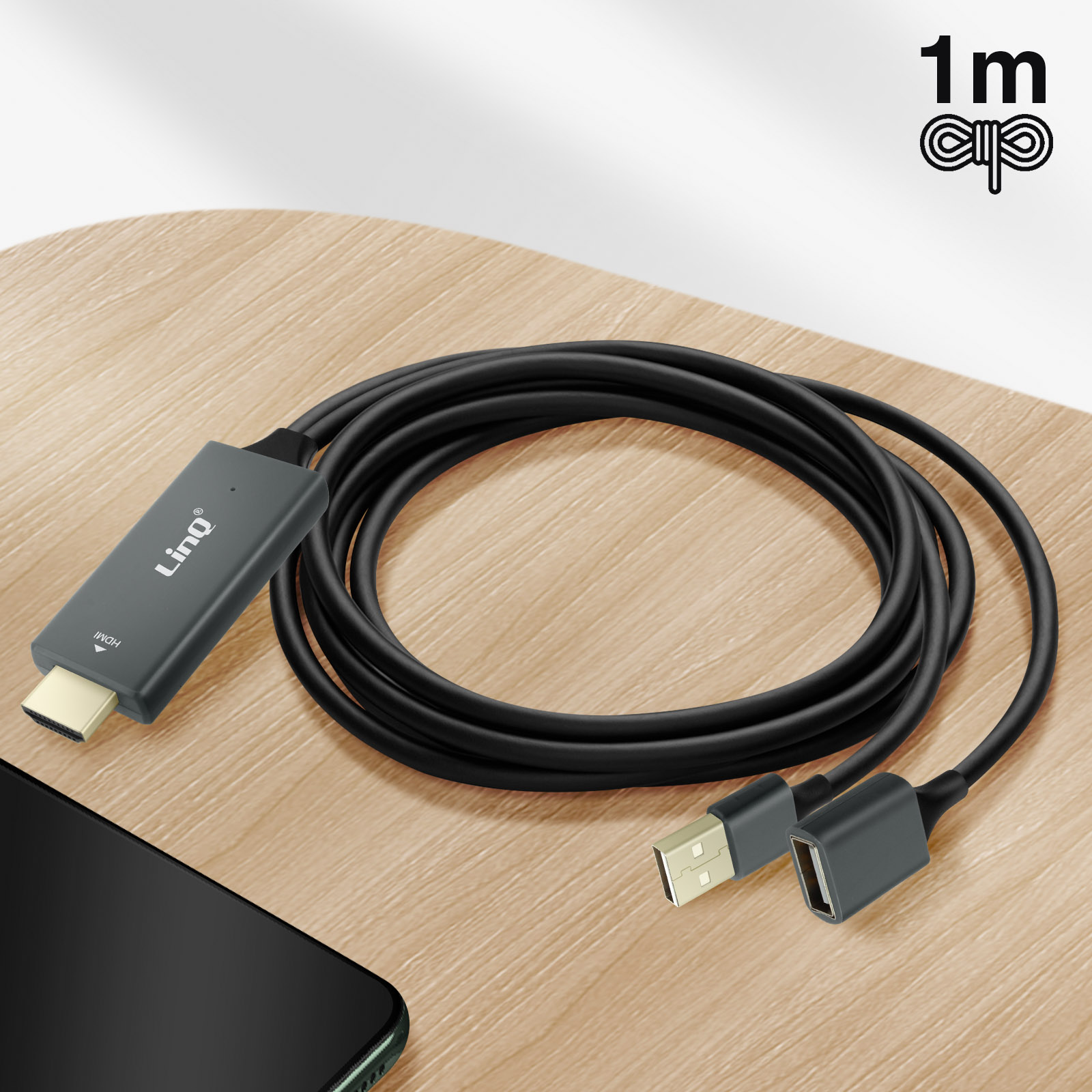 Cavo HDMI a USB nero per trasferimento dati, su un tavolo di legno. Smartphone nell'angolo.