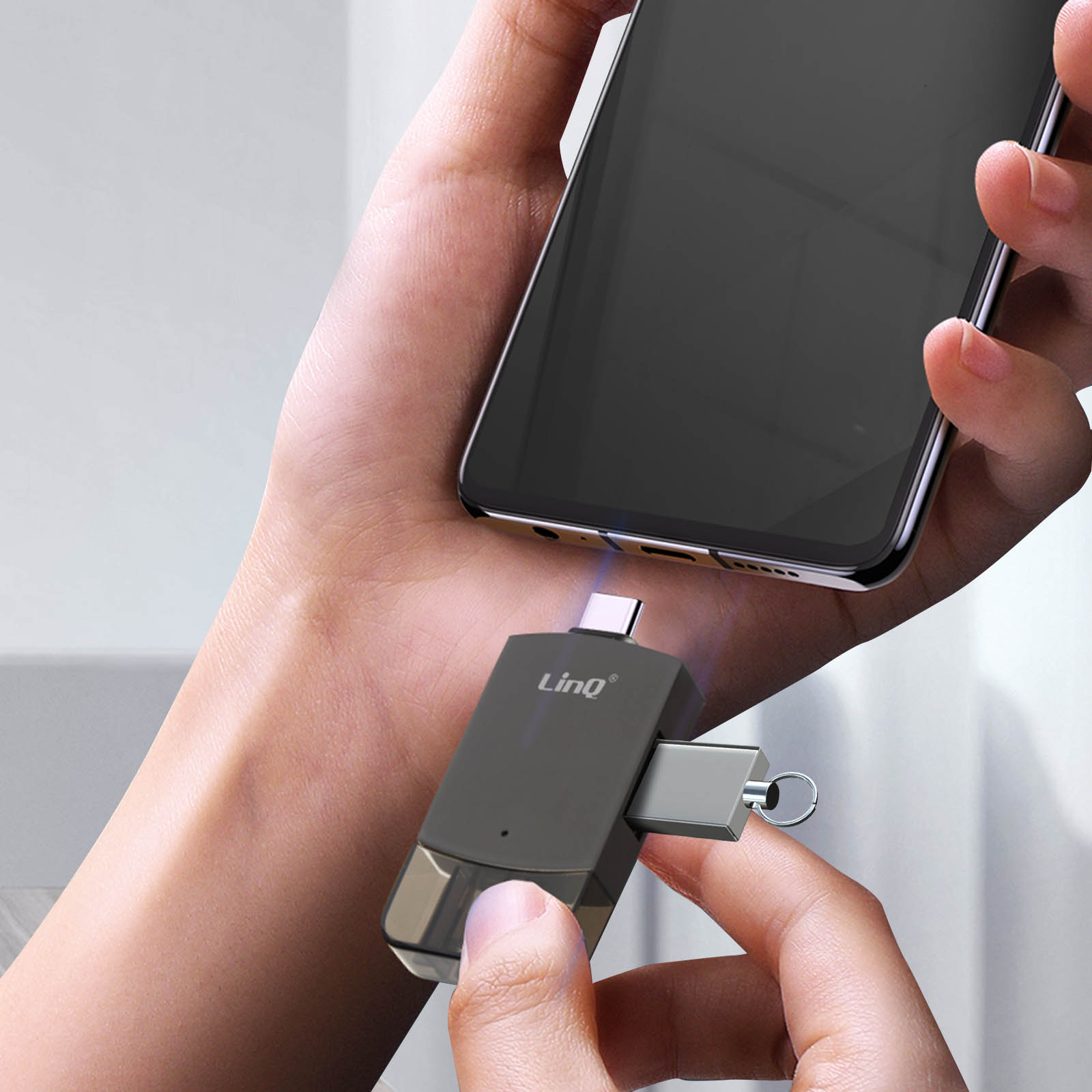 Personne tenant un téléphone et un adaptateur USB-C noir à côté.