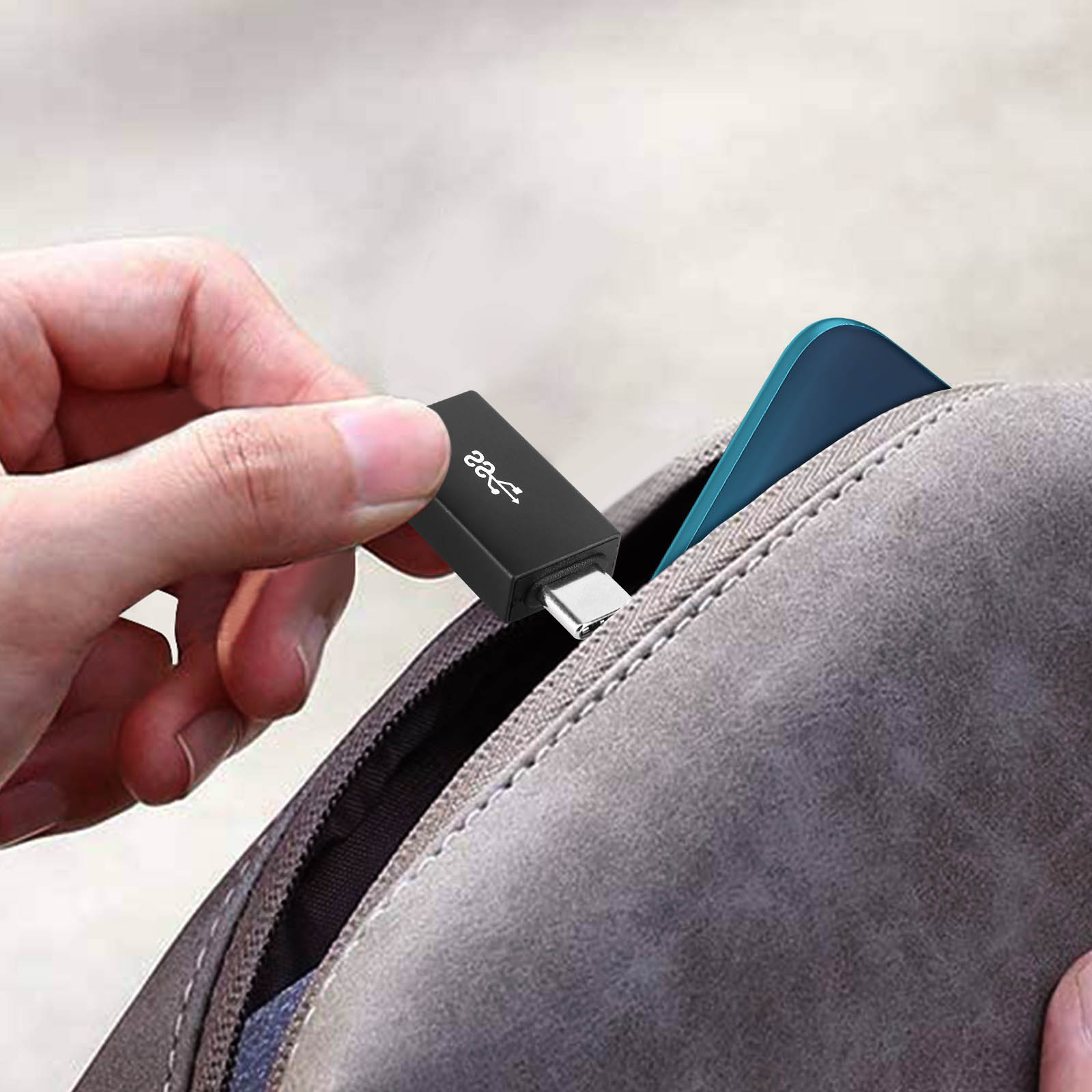 Mano che tiene un adattatore USB-C, mostrato in una tasca. Telefono visibile sullo sfondo.