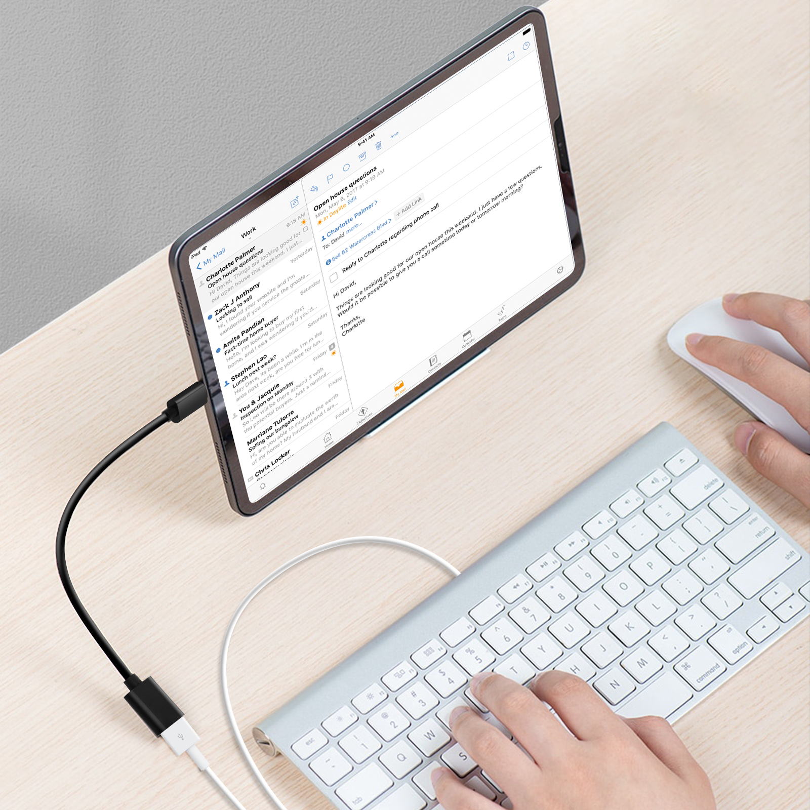 Tablet collegato a tastiera e mouse, che mostra e-mail su una scrivania in legno chiaro.