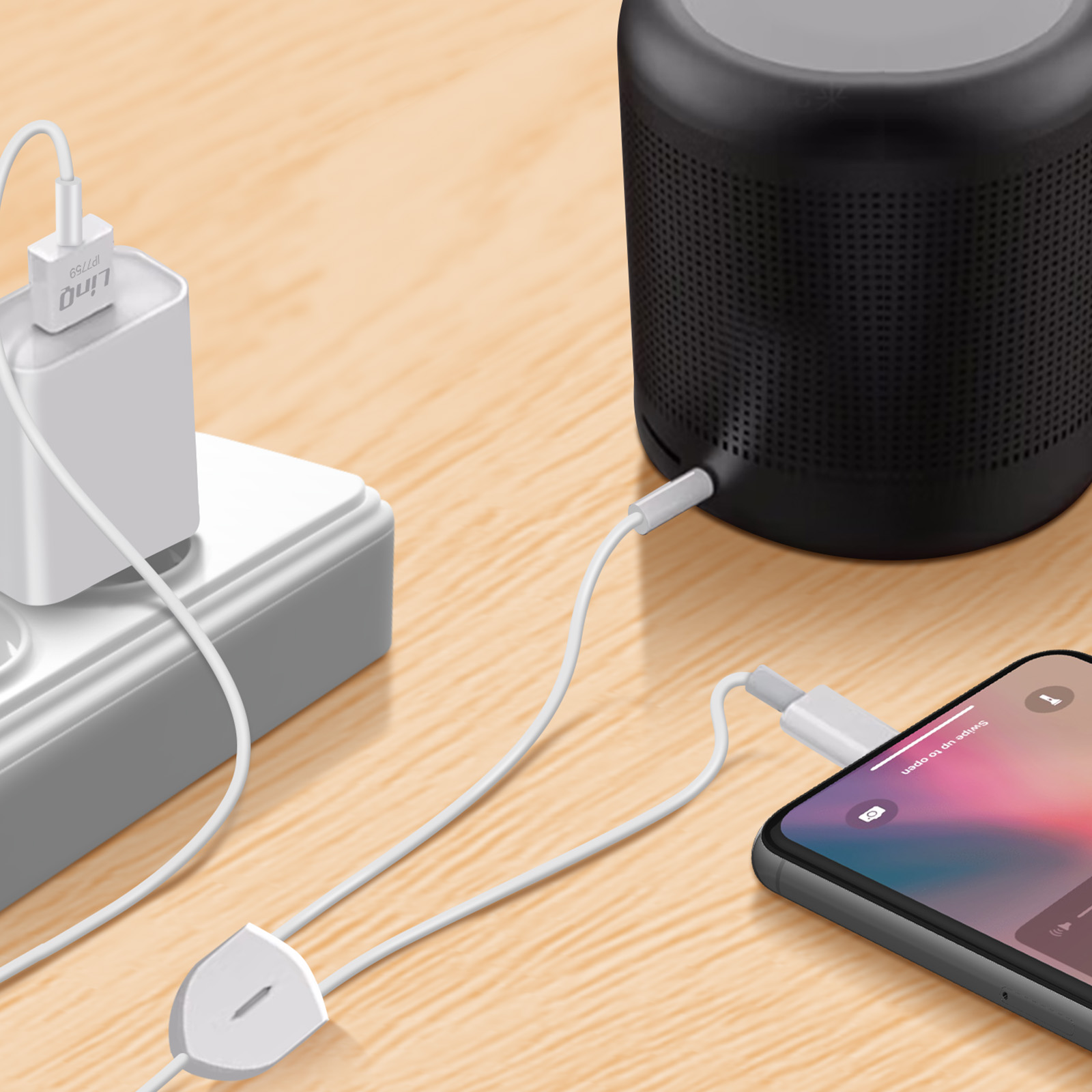 Telefon wird mit weißem Kabel aufgeladen, Lautsprecher und Wandladegerät auf Holzoberfläche.