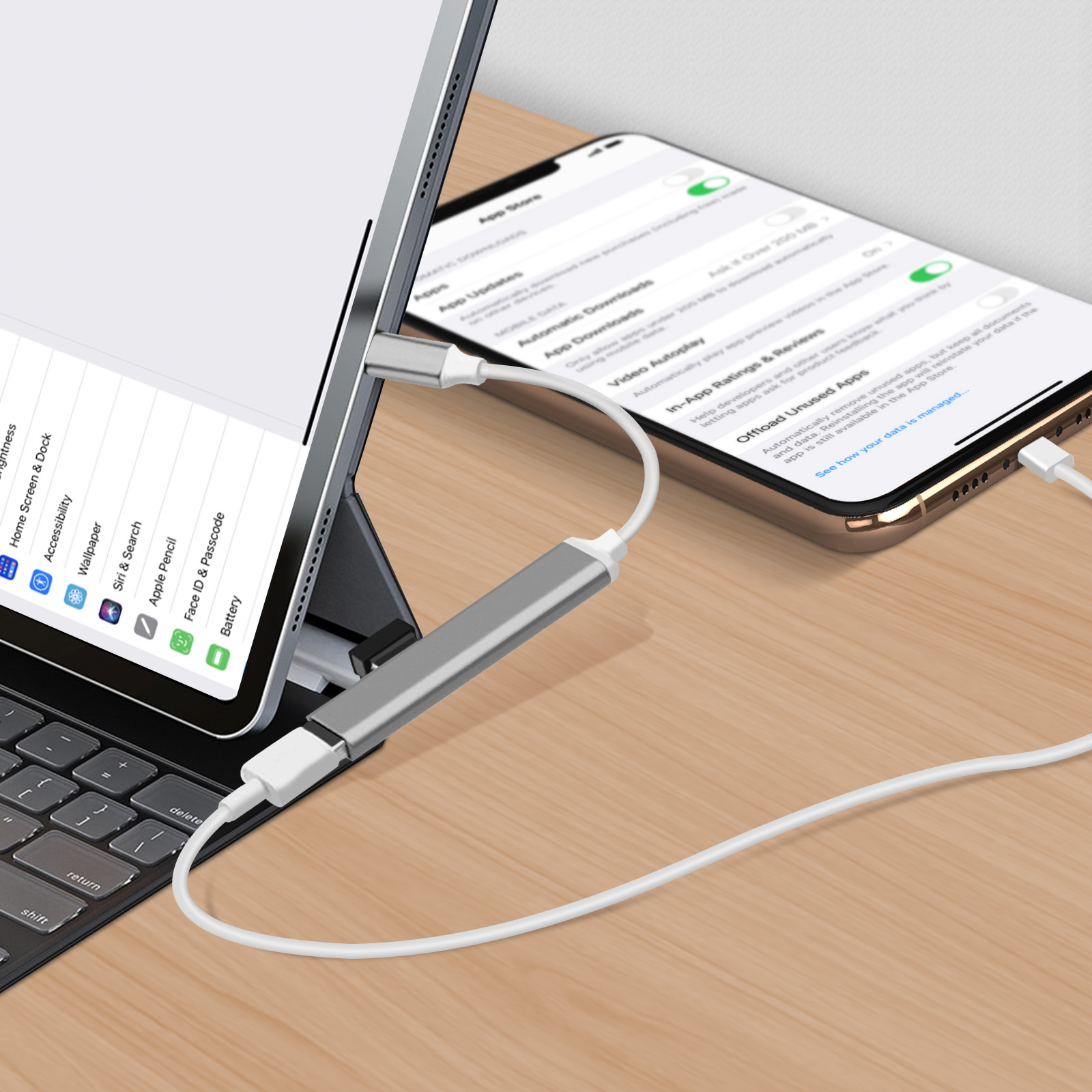 Une tablette et un téléphone sont connectés avec un câble blanc à un adaptateur gris sur une table en bois.
