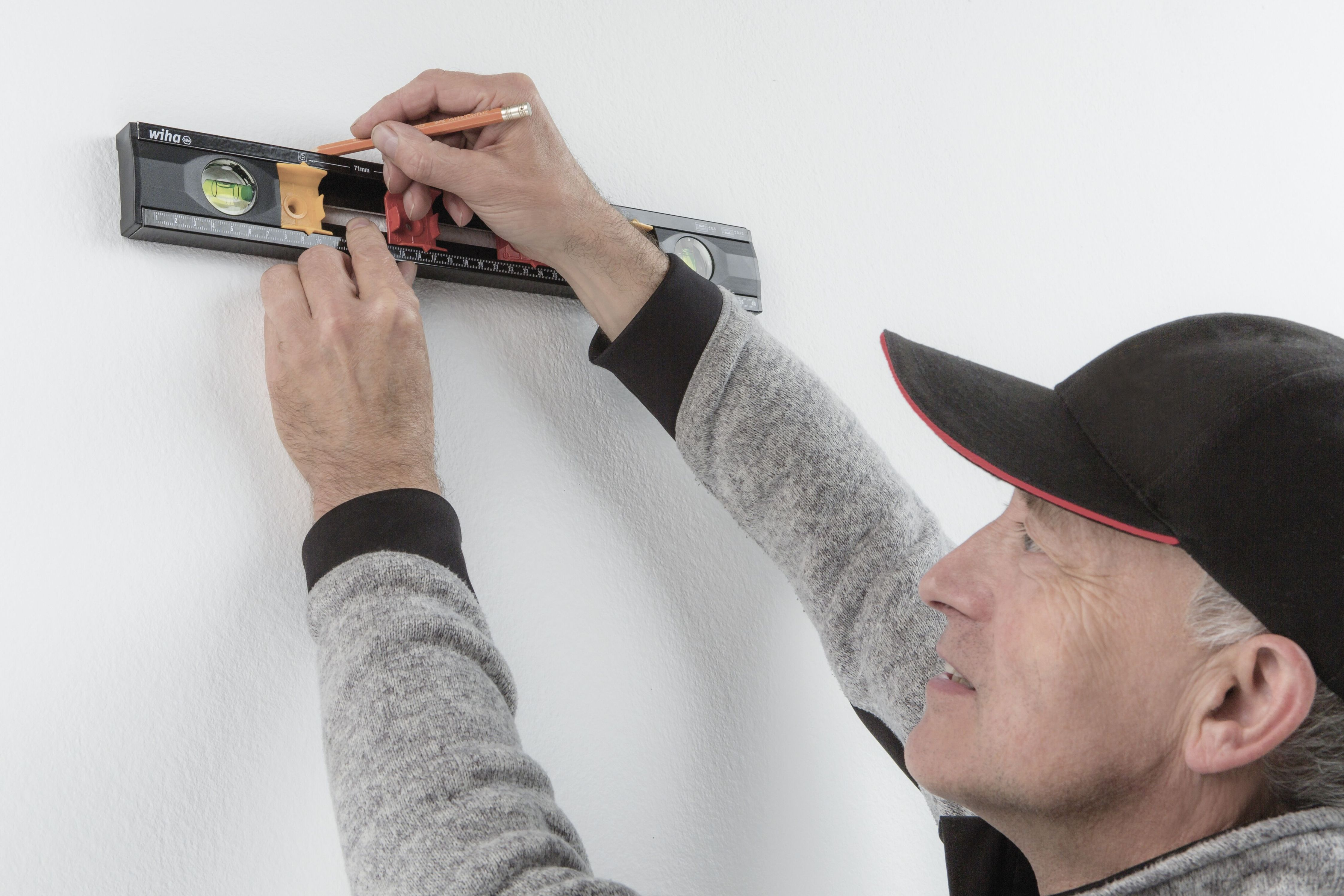 Ein Mann benutzt eine Wasserwaage an einer weißen Wand und hält einen Bleistift.