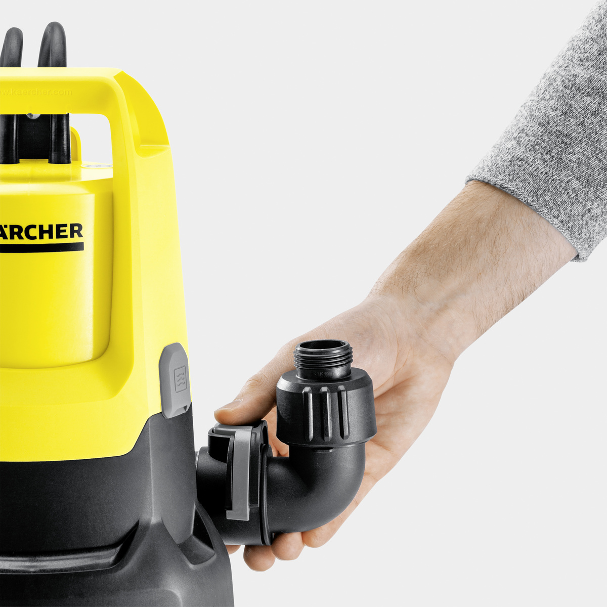 Żółto-czarna pompa zatapialna. Ręka łączy czarną rurę z pompą.