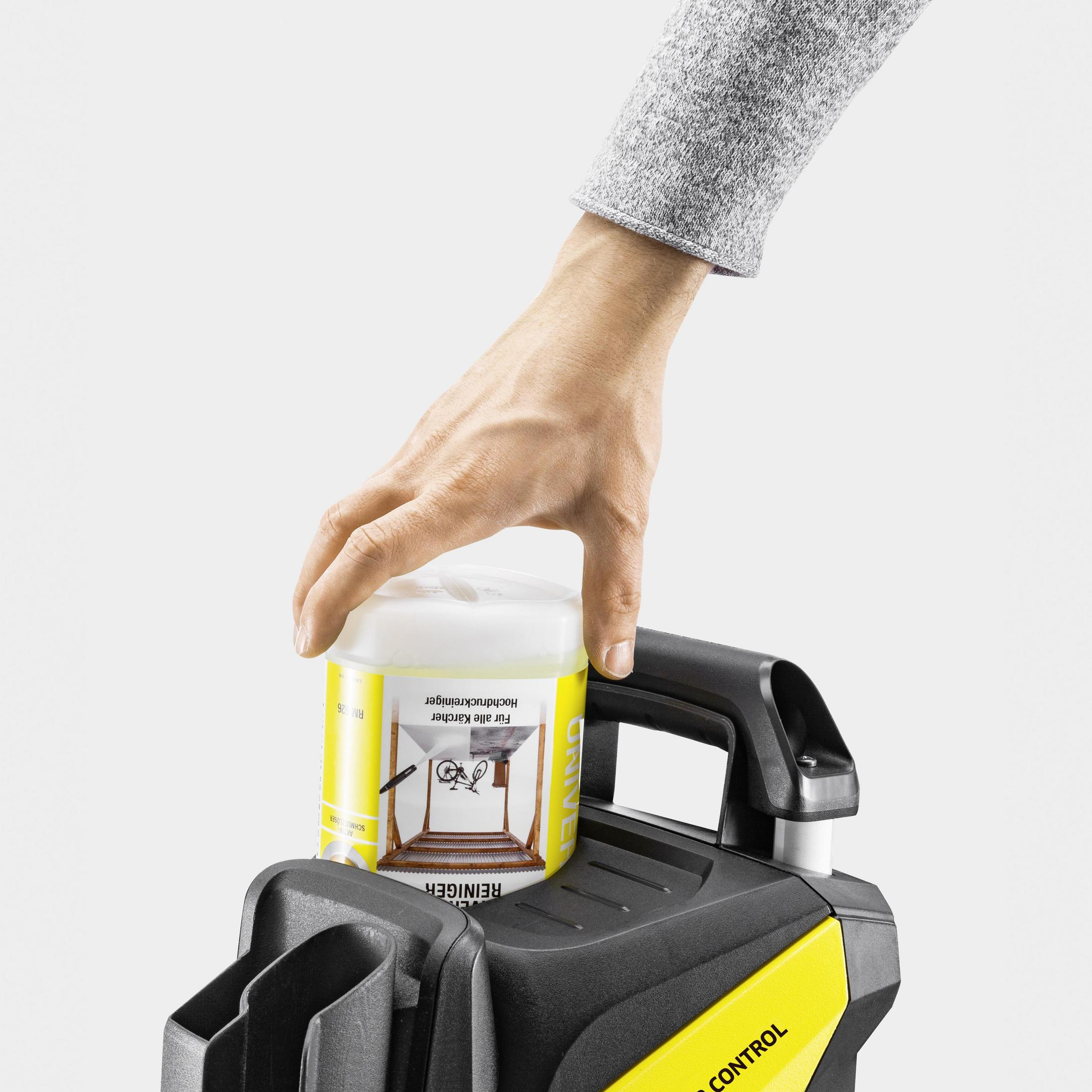 La mano de una persona colocando un producto de limpieza en una máquina de limpieza negra y amarilla.