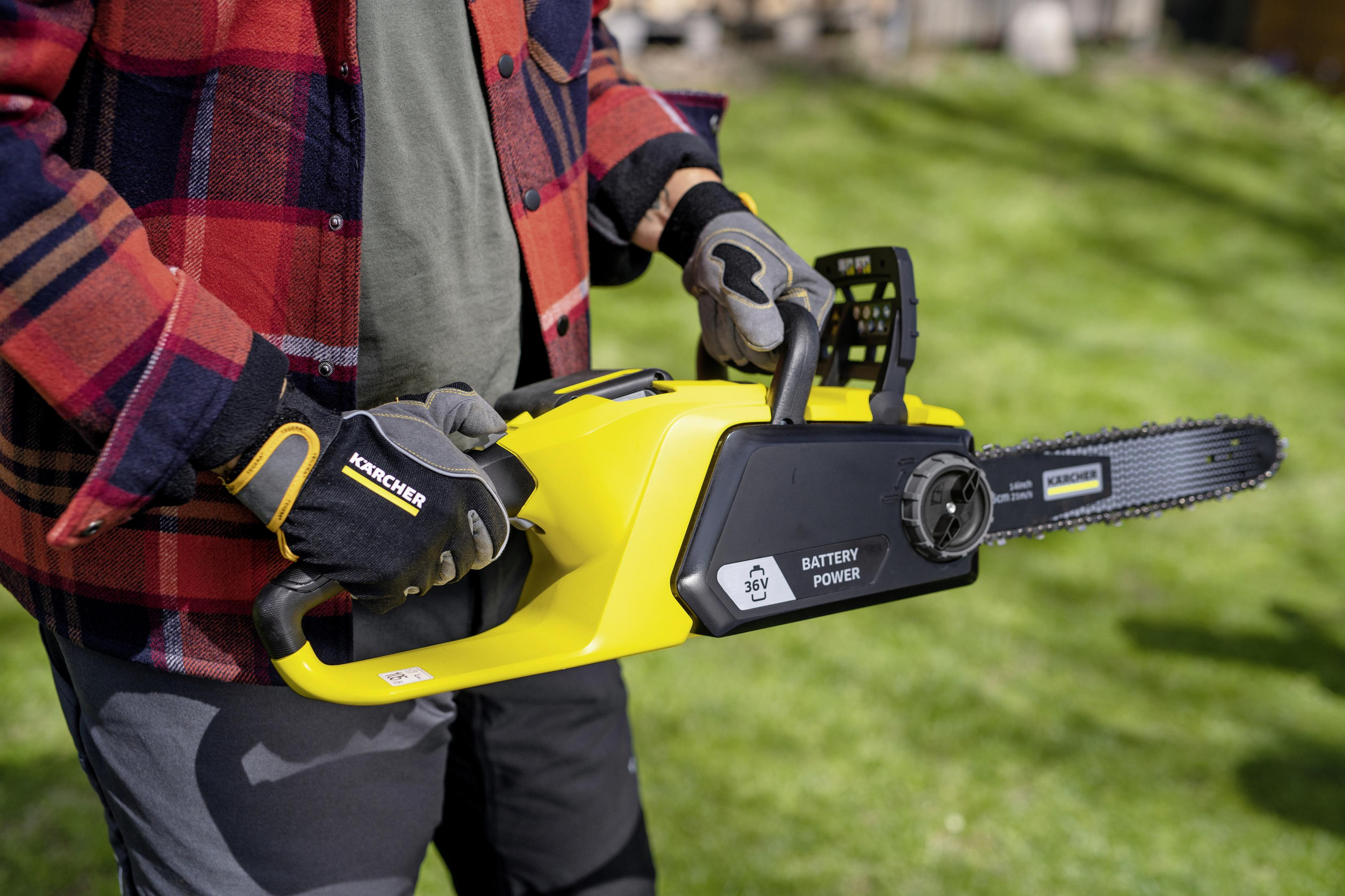 Osoba w rękawicach i czerwonej koszuli w kratę trzymająca żółtą piłę łańcuchową w ogrodzie.