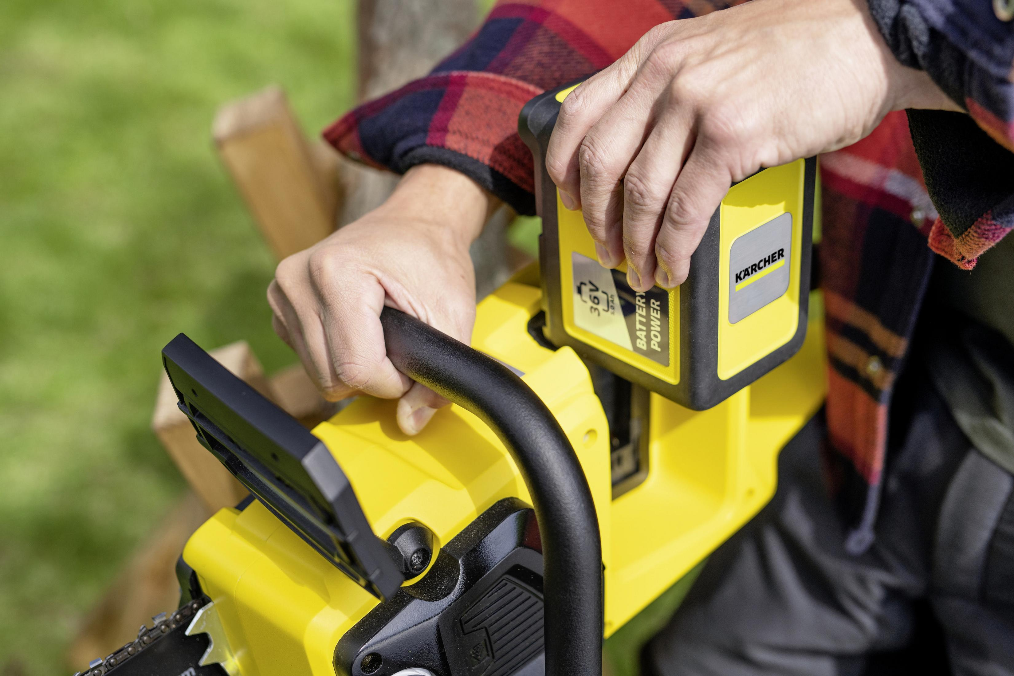 Osoba wkłada żółtą baterię do żółto-czarnej piły łańcuchowej.