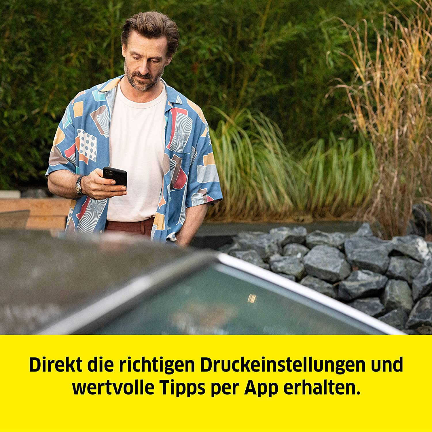 Mężczyzna spogląda na telefon na zewnątrz, żółty tekst: ustawienia drukowania i wskazówki przez aplikację.
