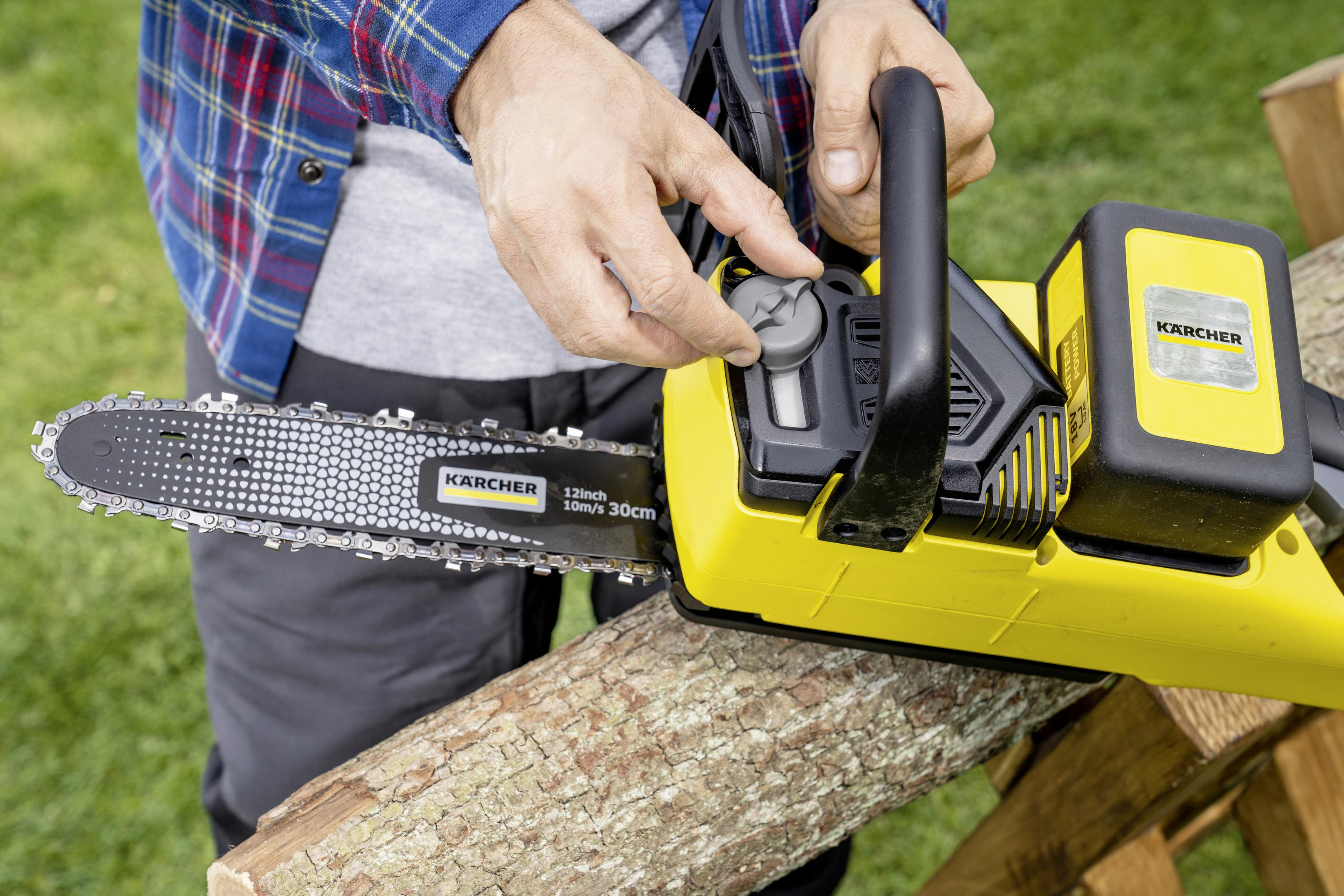 Osoba używająca żółtej piły łańcuchowej Karcher do cięcia drewna na drewnianym stojaku.