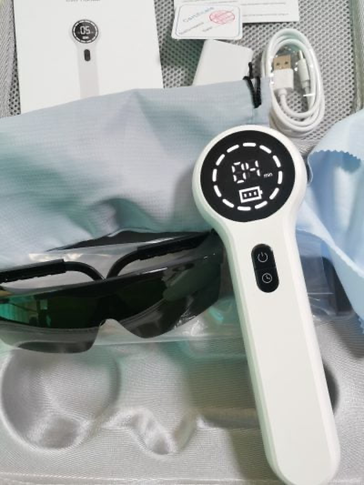Weißes Gerät mit Bildschirm, Schutzbrille und Ladekabel. Das Paket enthält Zubehör.
