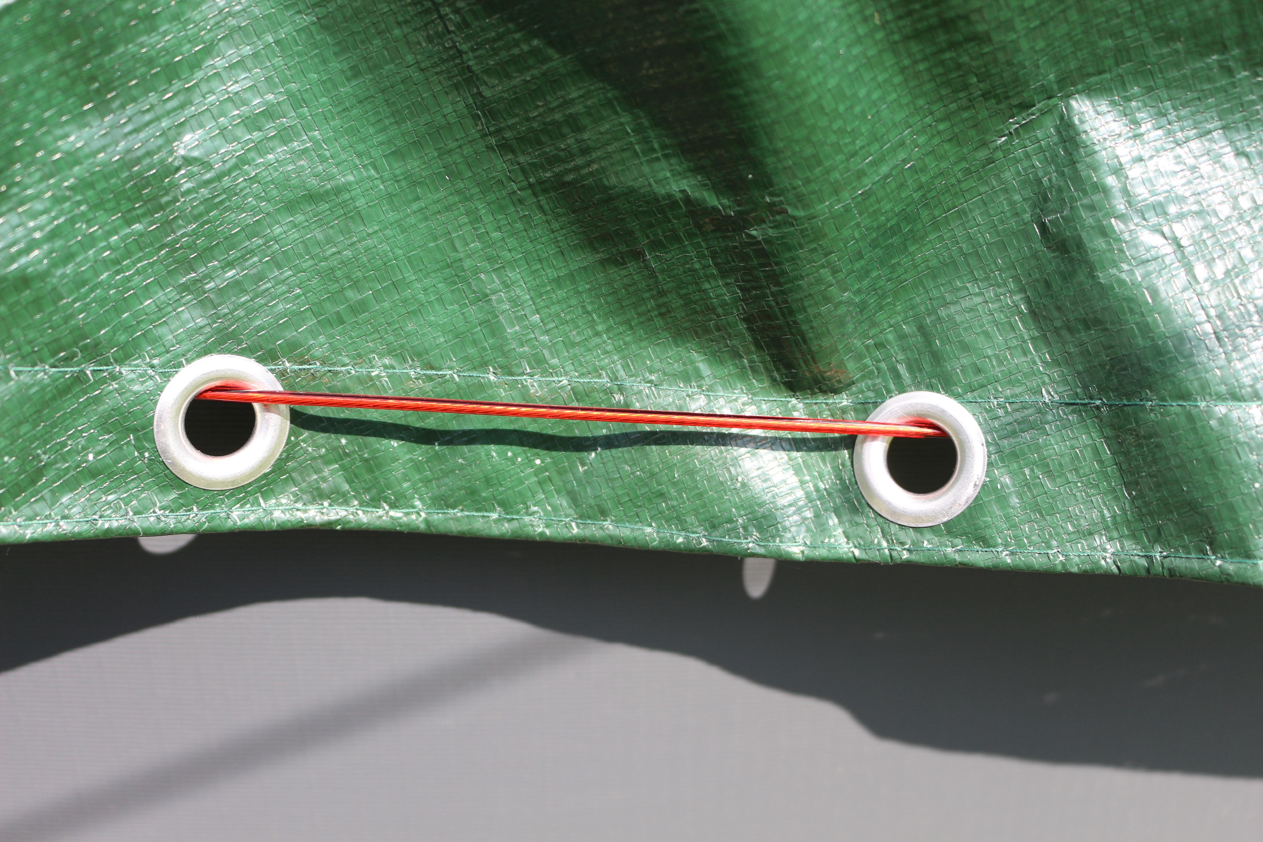 Grüne Plane mit zwei Ösen und roter Schnur. Grauer Hintergrund.