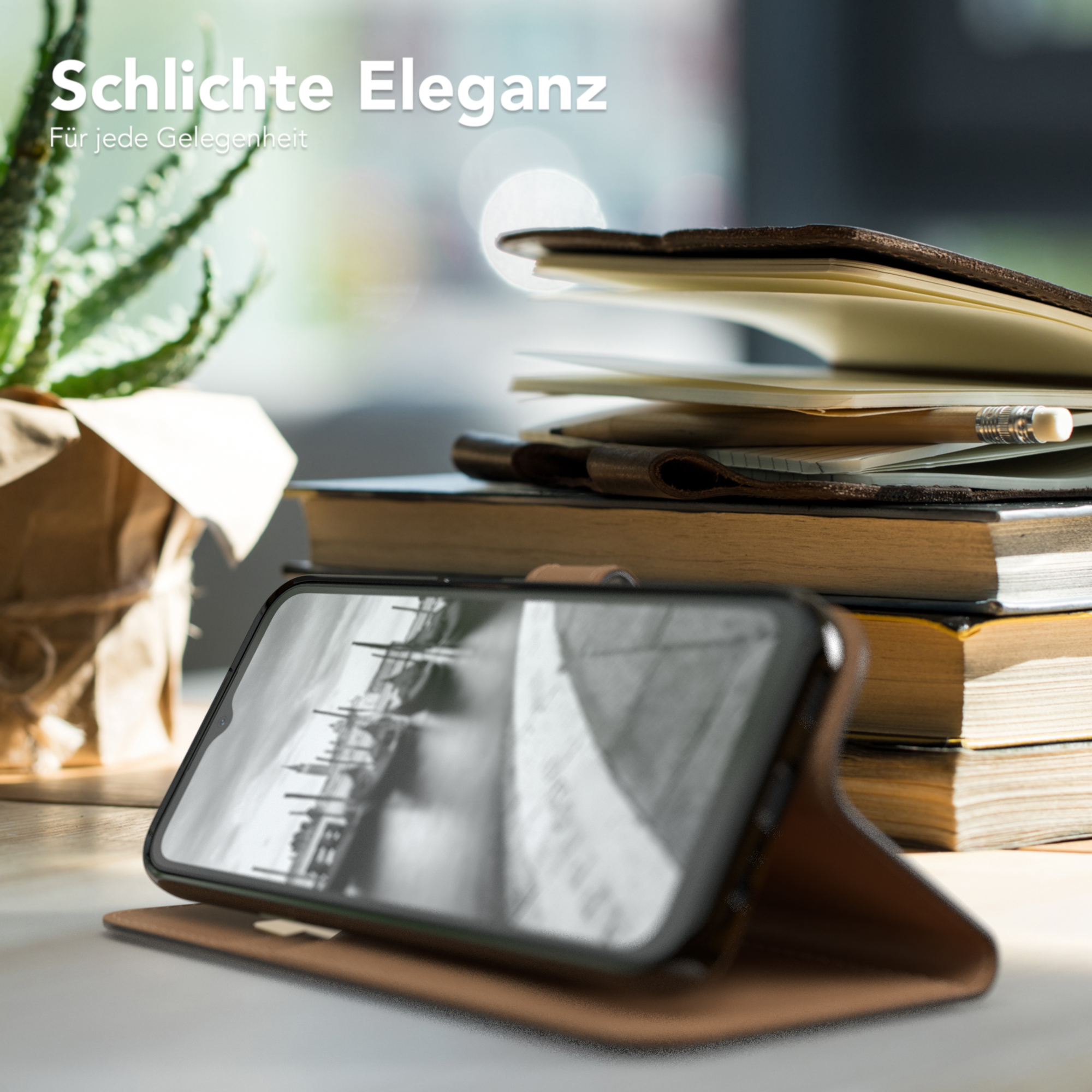 Ein Smartphone in einer braunen Lederhülle liegt auf einem Schreibtisch neben Büchern und einer Pflanze.