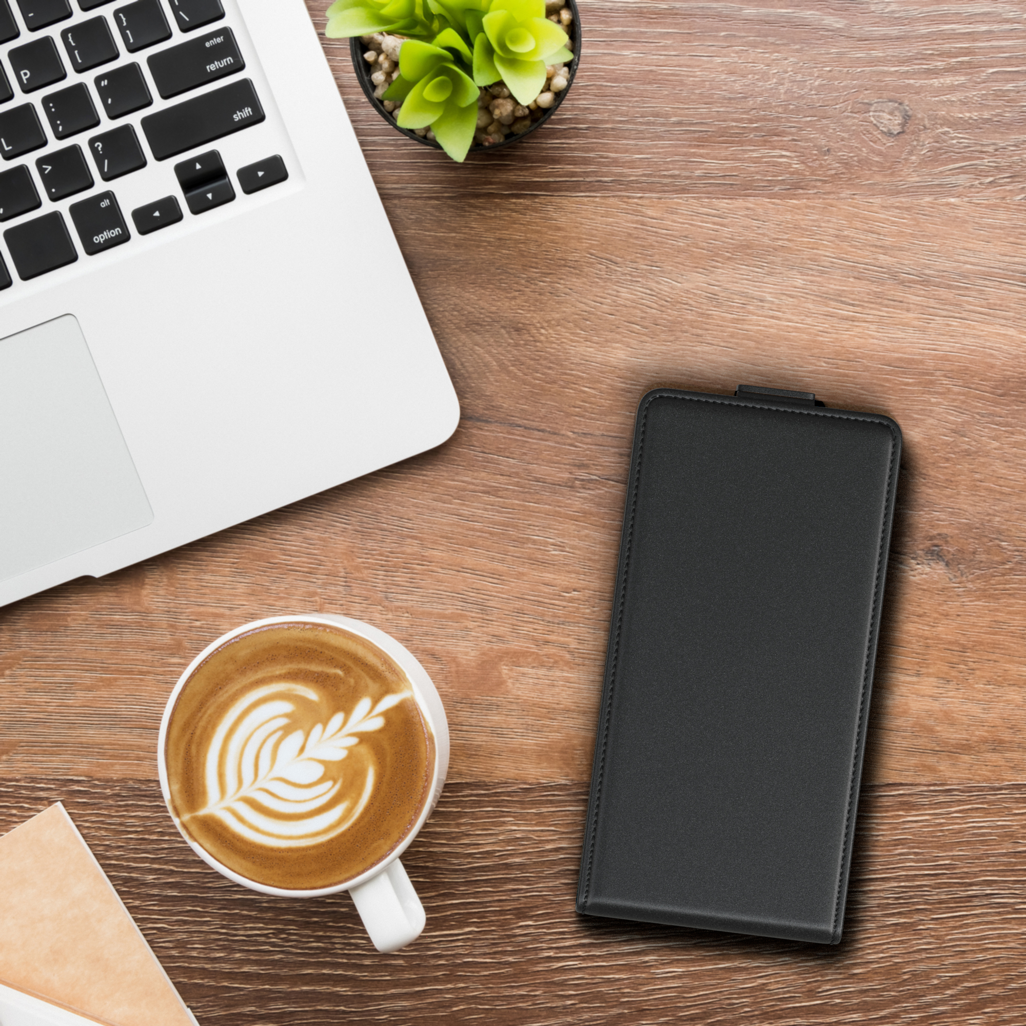 Laptop, Kaffeetasse, Stift und Handyhülle auf einem Holztisch, Draufsicht.