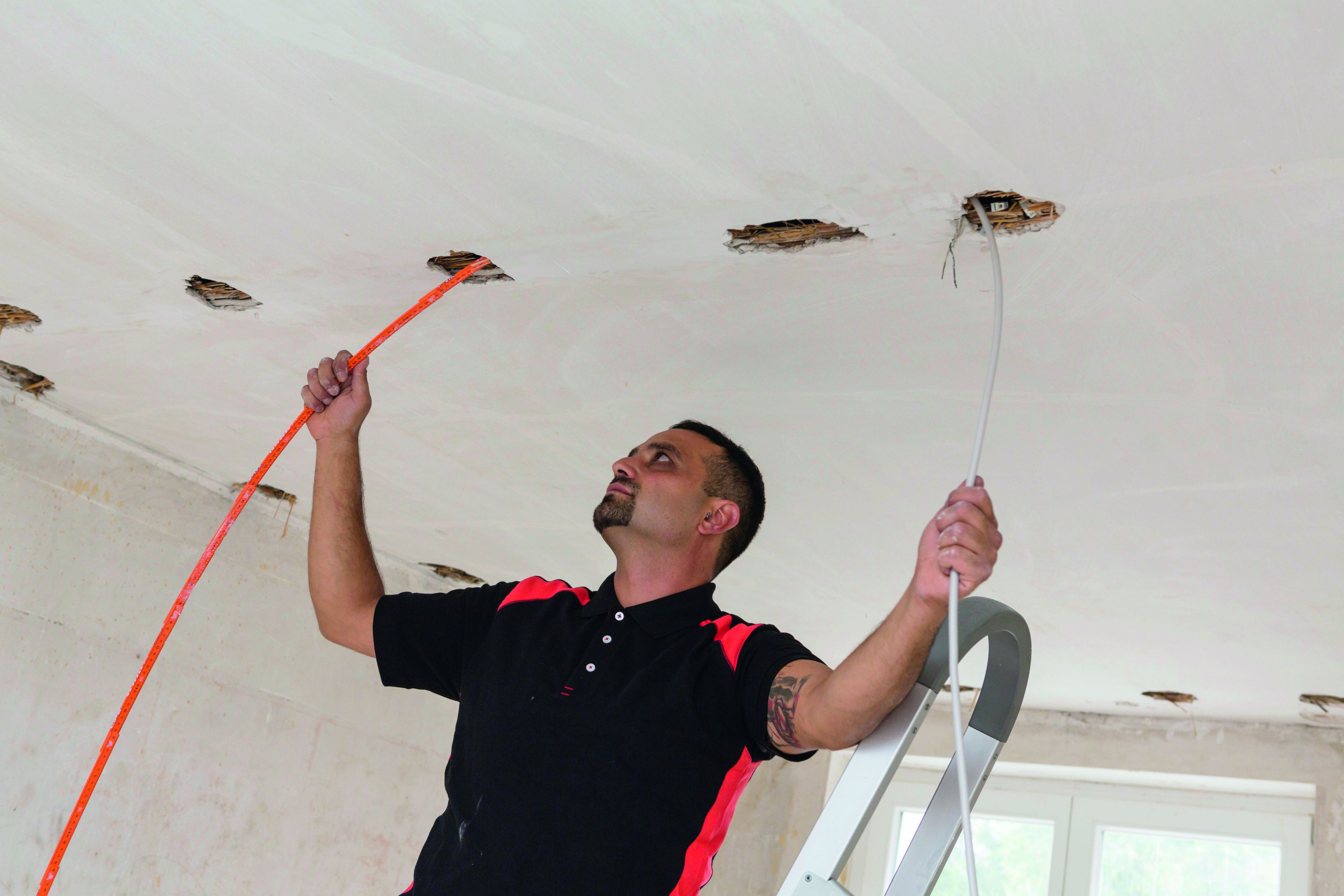 Ein Mann installiert Kabel in einer Decke, trägt ein schwarzes Hemd.