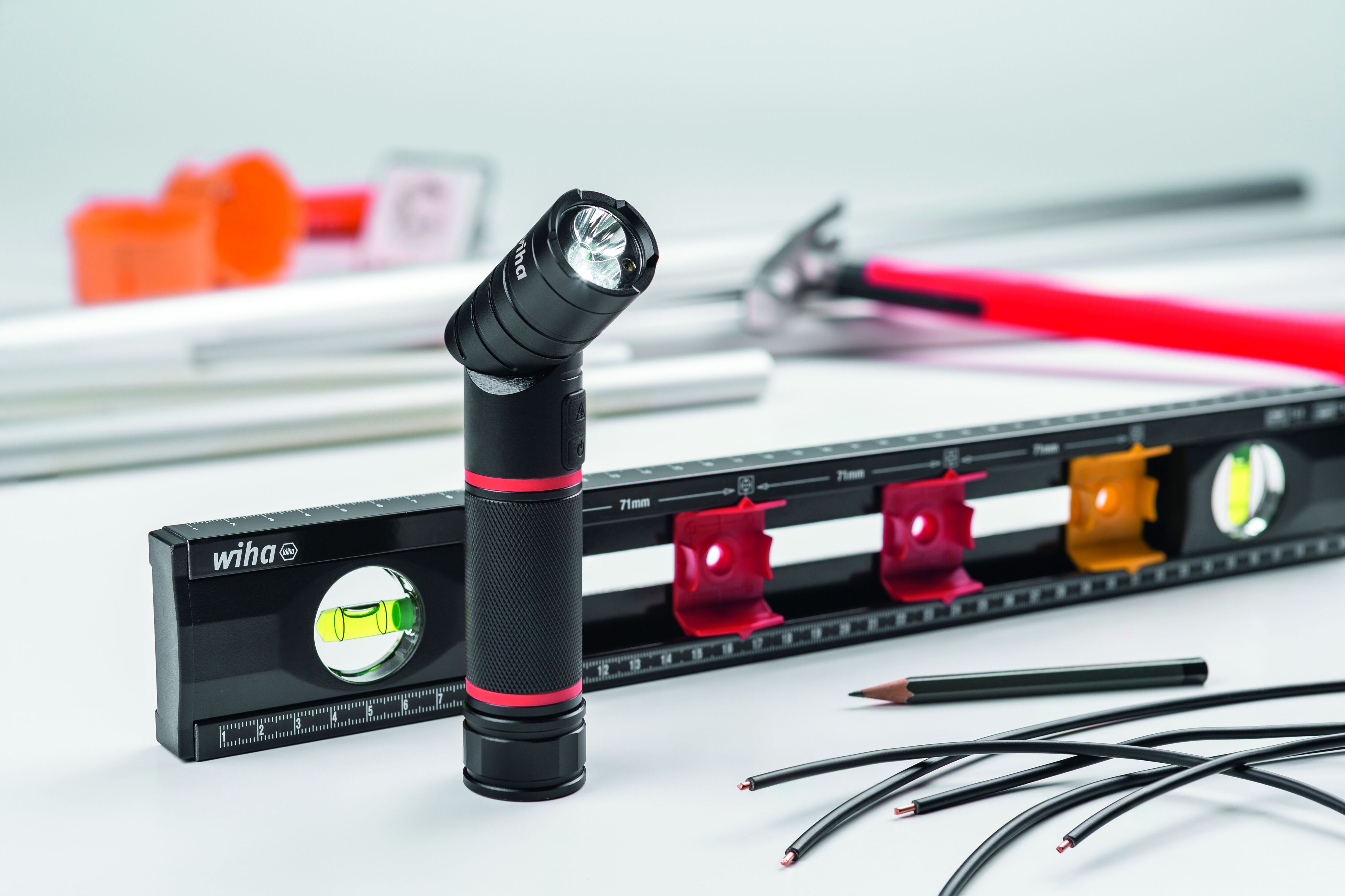 Schwarz-rote Taschenlampe nach oben gerichtet mit Wasserwaage und Bleistift.