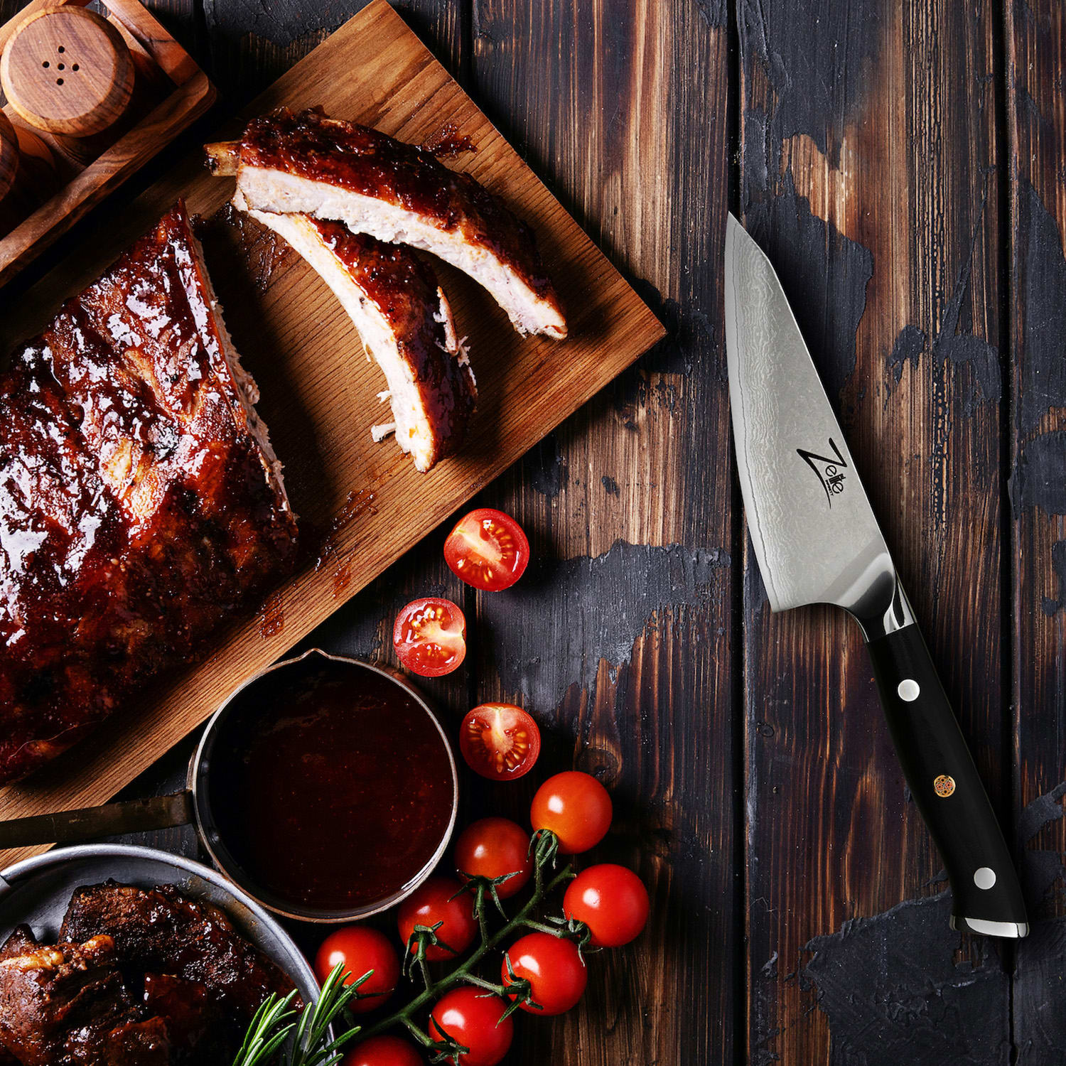 Ein hölzernes Schneidebrett mit gegrillten Rippchen, Tomaten, einem Messer und Soße.