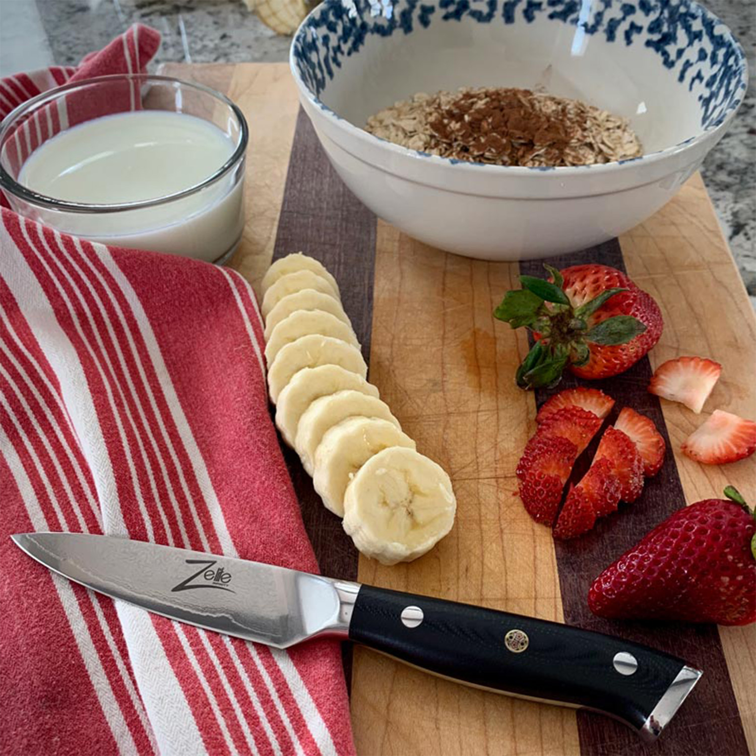 Ein Schneidebrett mit Zutaten für das Frühstück: Bananenscheiben, Erdbeeren, Haferflocken und ein Glas Milch.