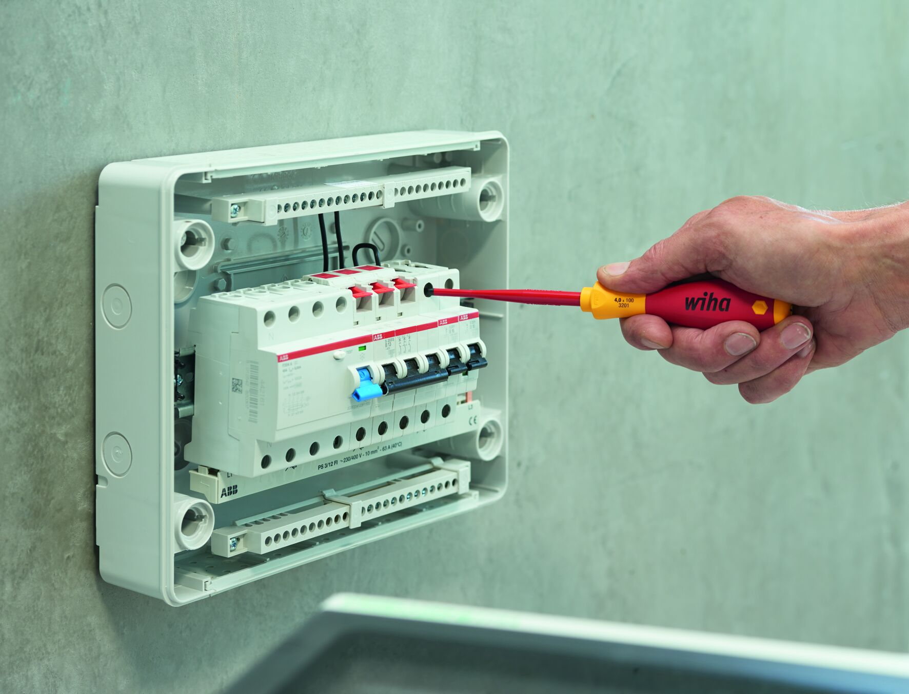 Panel elektryczny z czerwonymi i niebieskimi przełącznikami. Ręka trzymająca śrubokręt. Szara ściana.