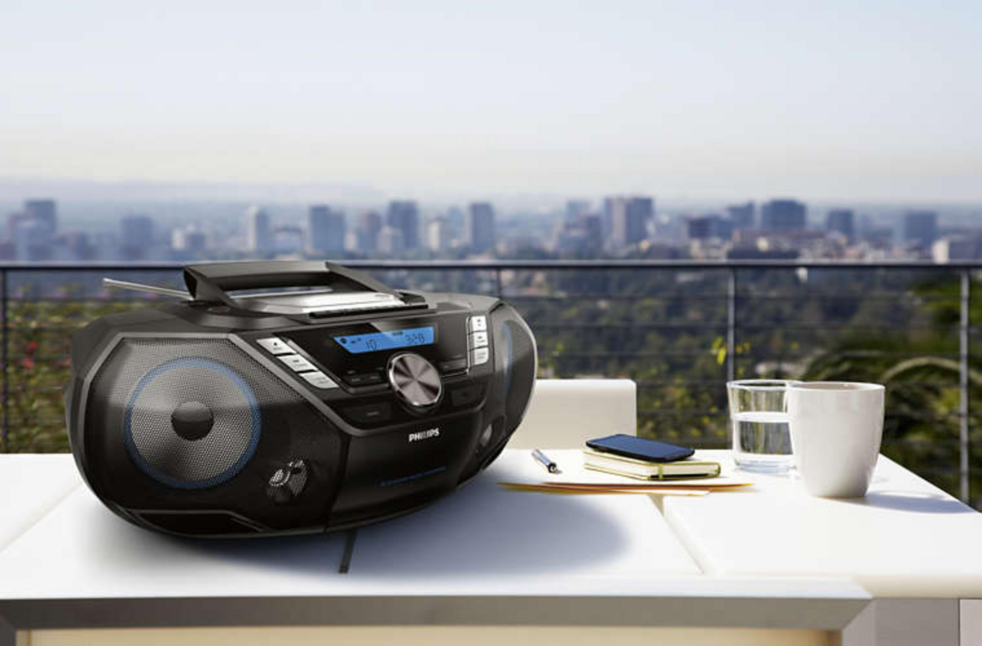 Una radio nera su un tavolo con un bicchiere, acqua e un telefono. Skyline sullo sfondo.