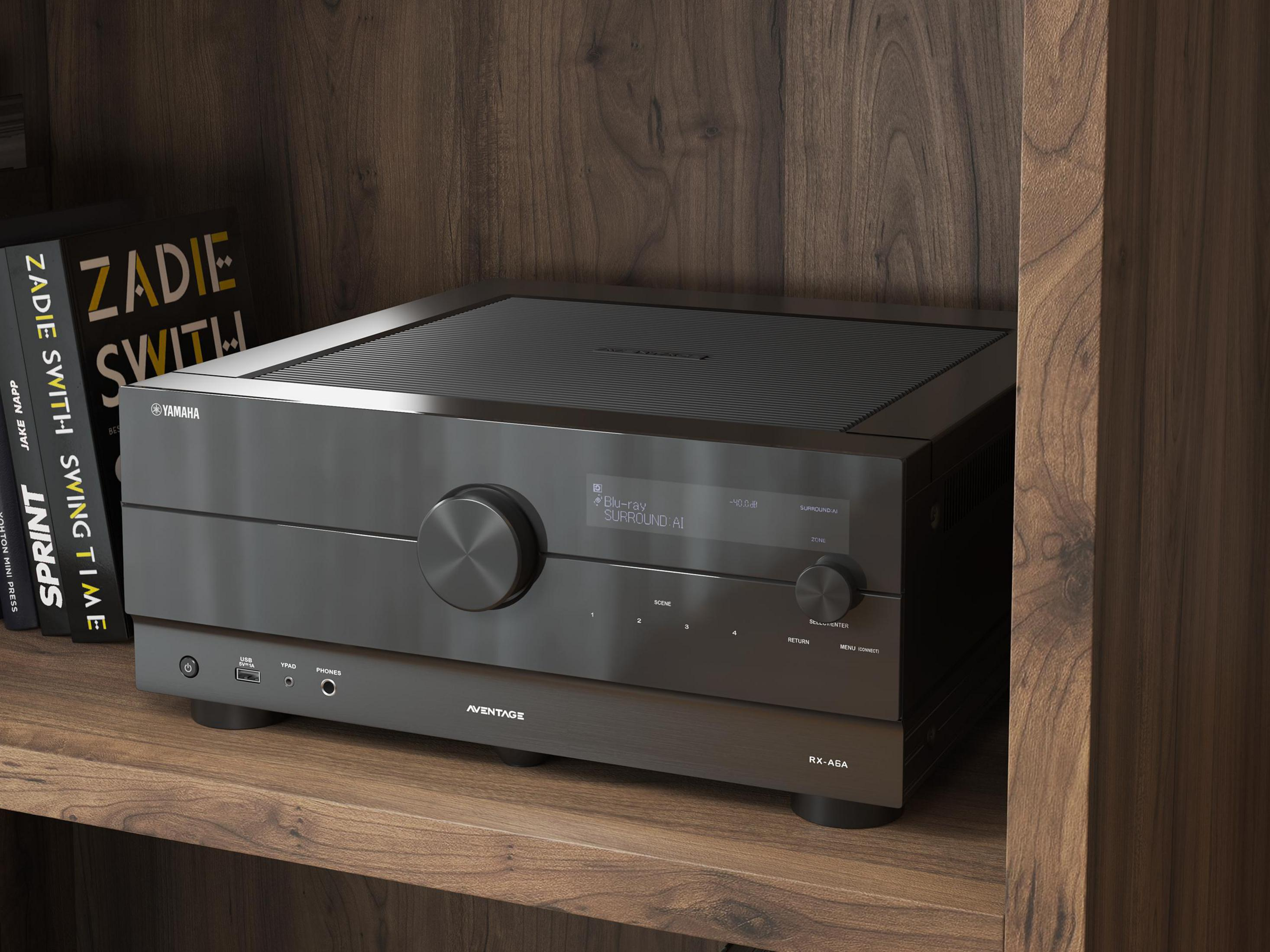 Ein schwarzer Yamaha AVENTAGE-Receiver steht auf einem Holzregal. Bücher sind links.