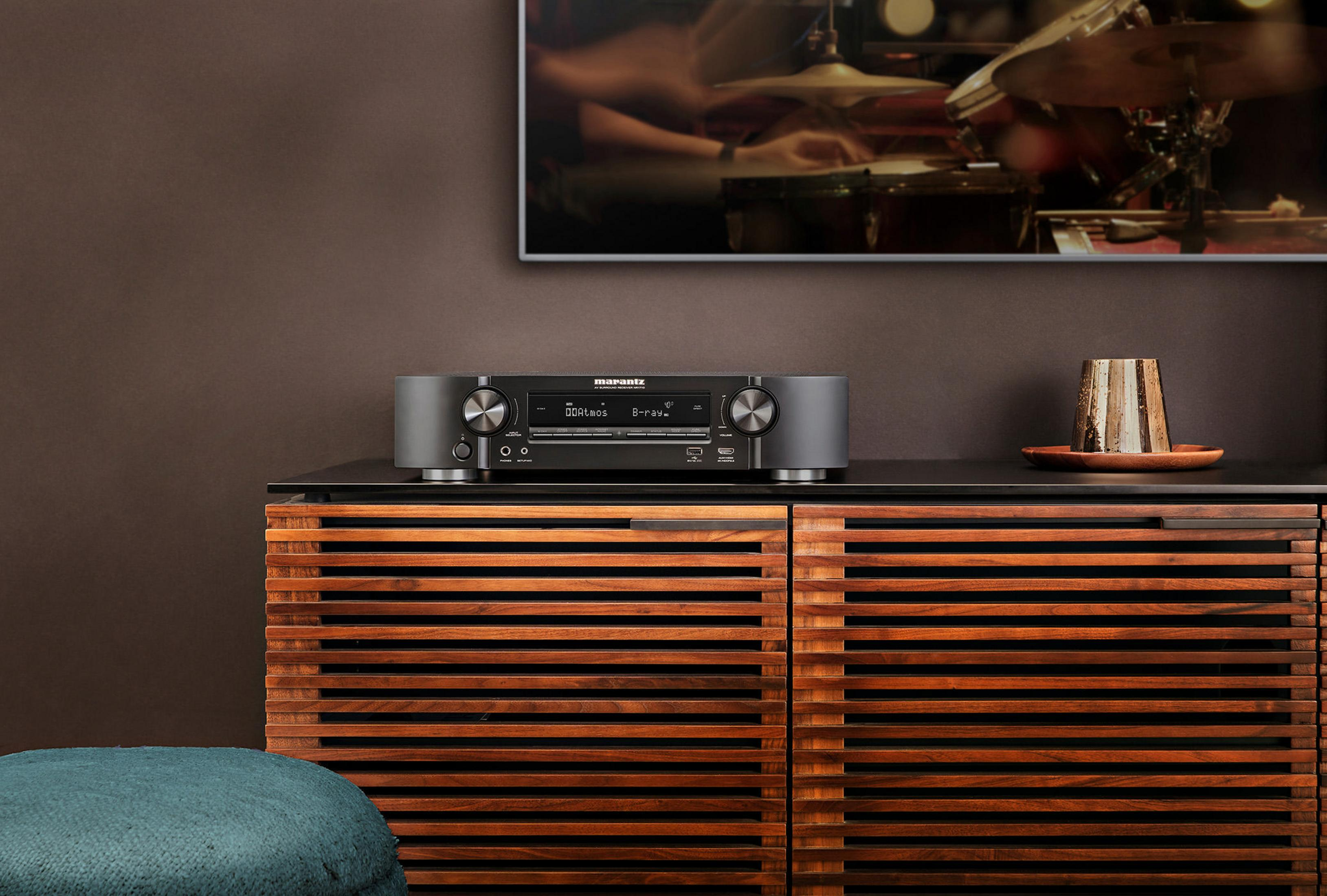 Ein moderner schwarz-silberner Stereo-Receiver auf einem Holzschrank mit einem Fernseher im Hintergrund.