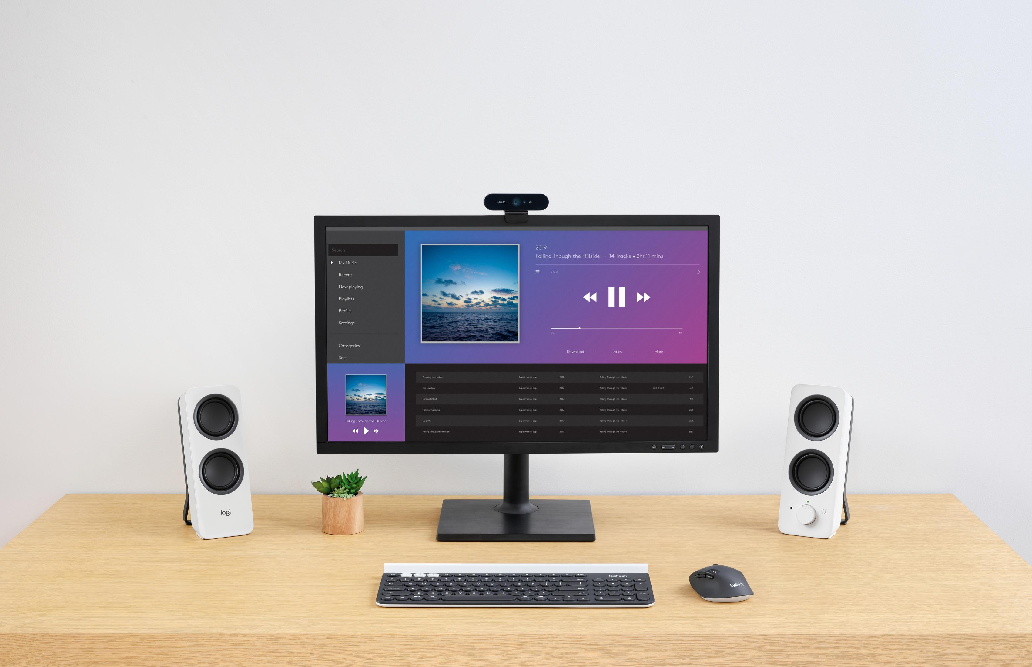 Escritorio con monitor que muestra una interfaz de reproductor de música, altavoces y teclado.