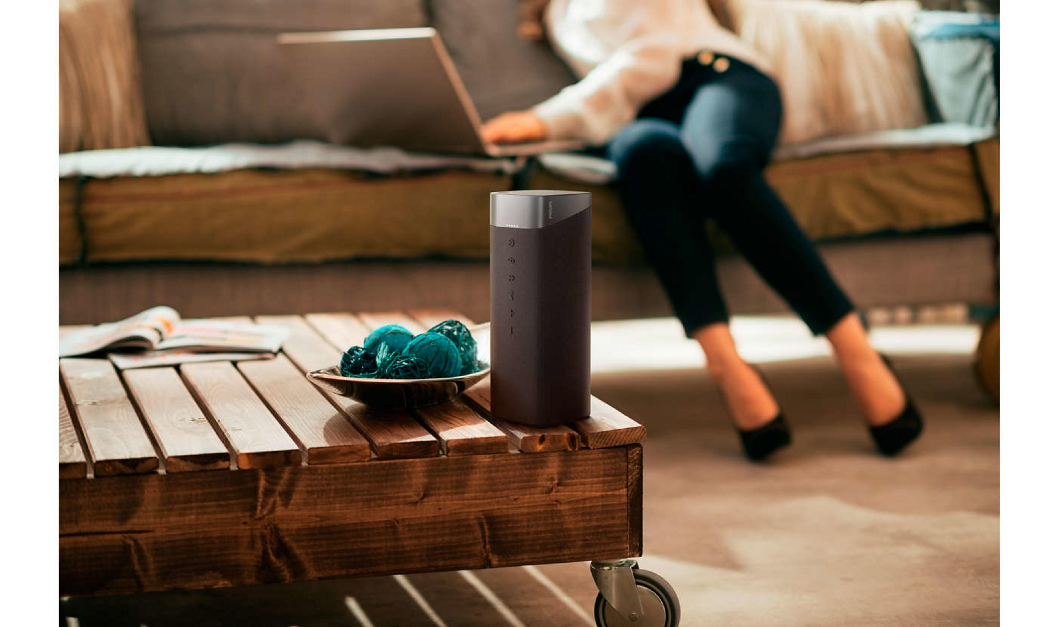 Czarny głośnik na drewnianym stole z laptopem i dekoracjami. Osoba korzysta z laptopa.