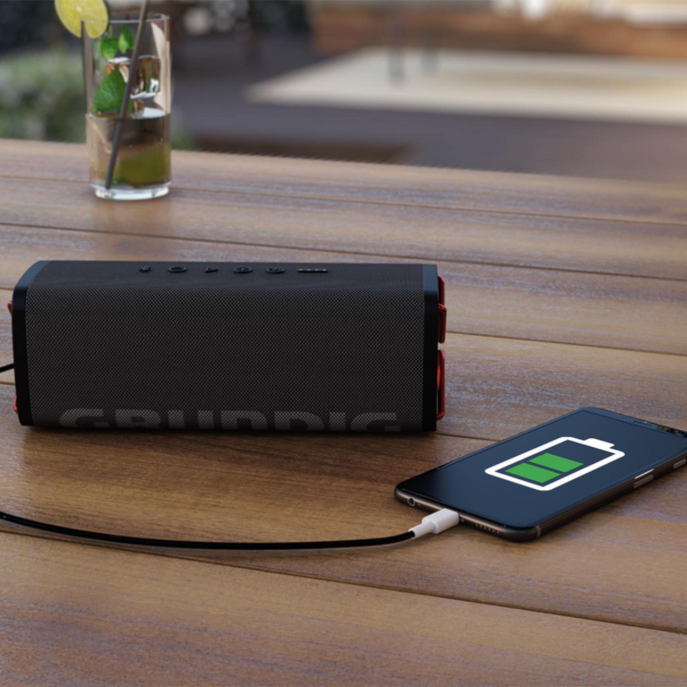 Czarny głośnik ładujący się na drewnianym stole obok telefonu z ikoną ładowania.