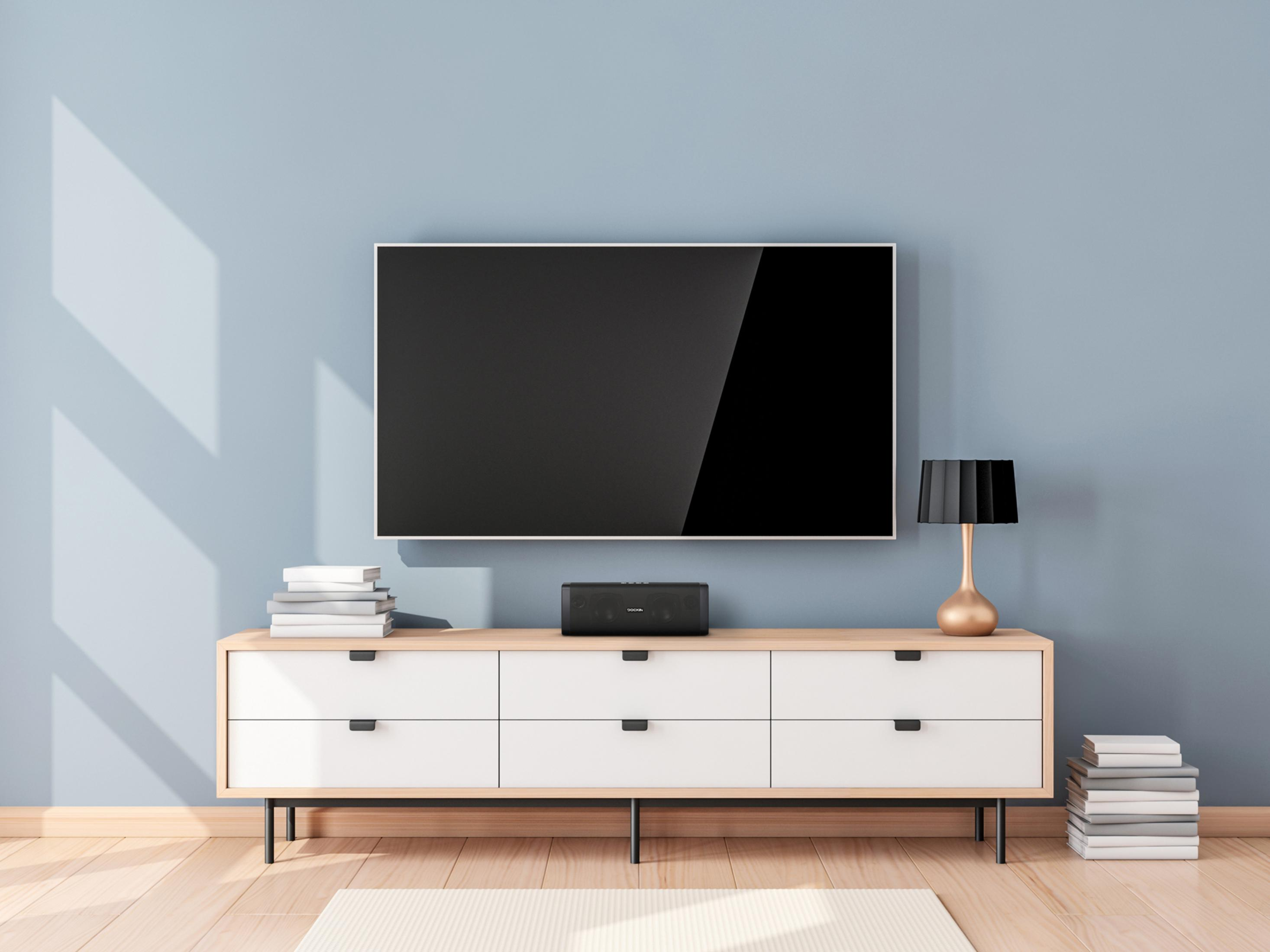Ein Fernseher ist an einer hellblauen Wand über einem weißen Schrank mit einer schwarzen Soundbar montiert.