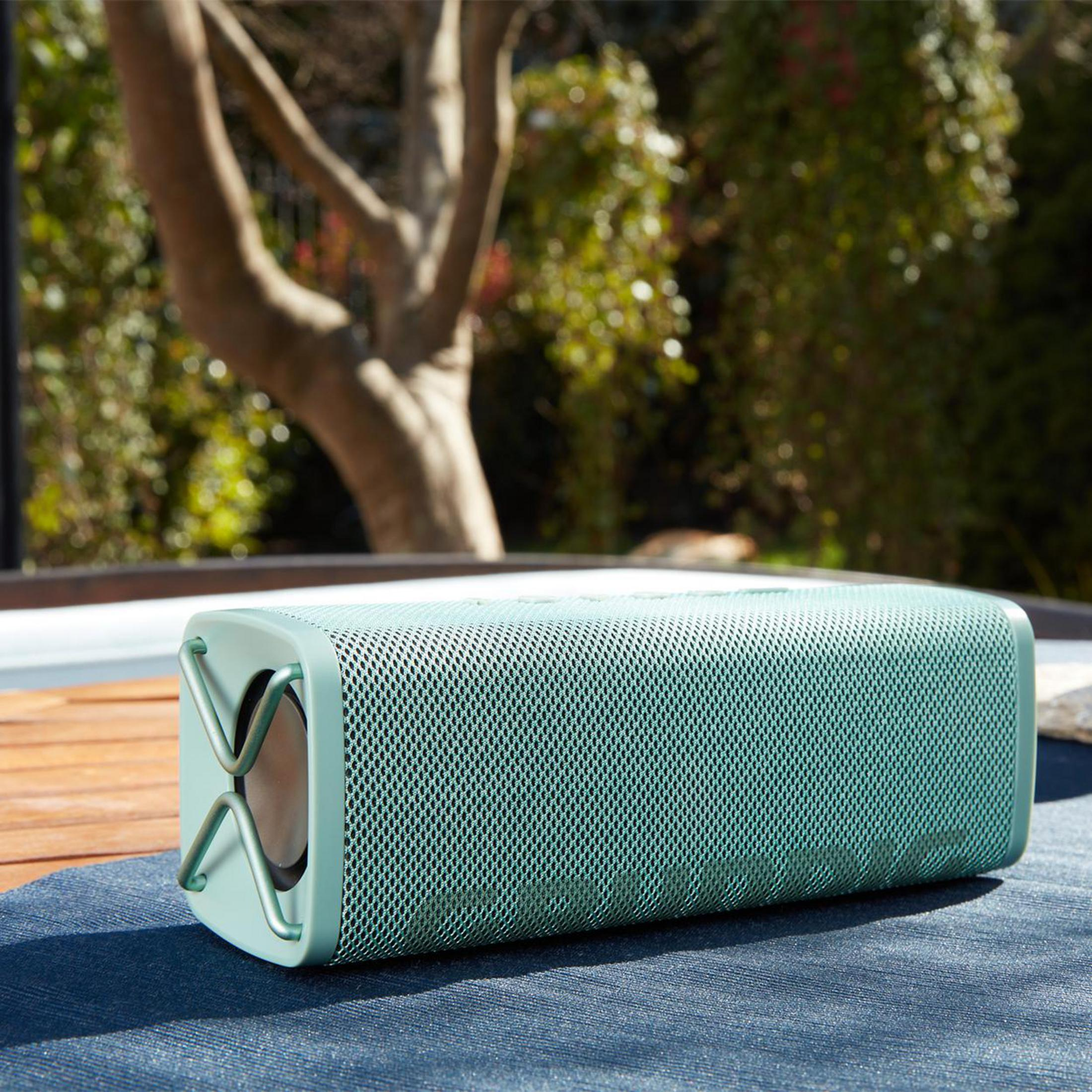 Zielony głośnik na stole, na zewnątrz w słonecznym otoczeniu.