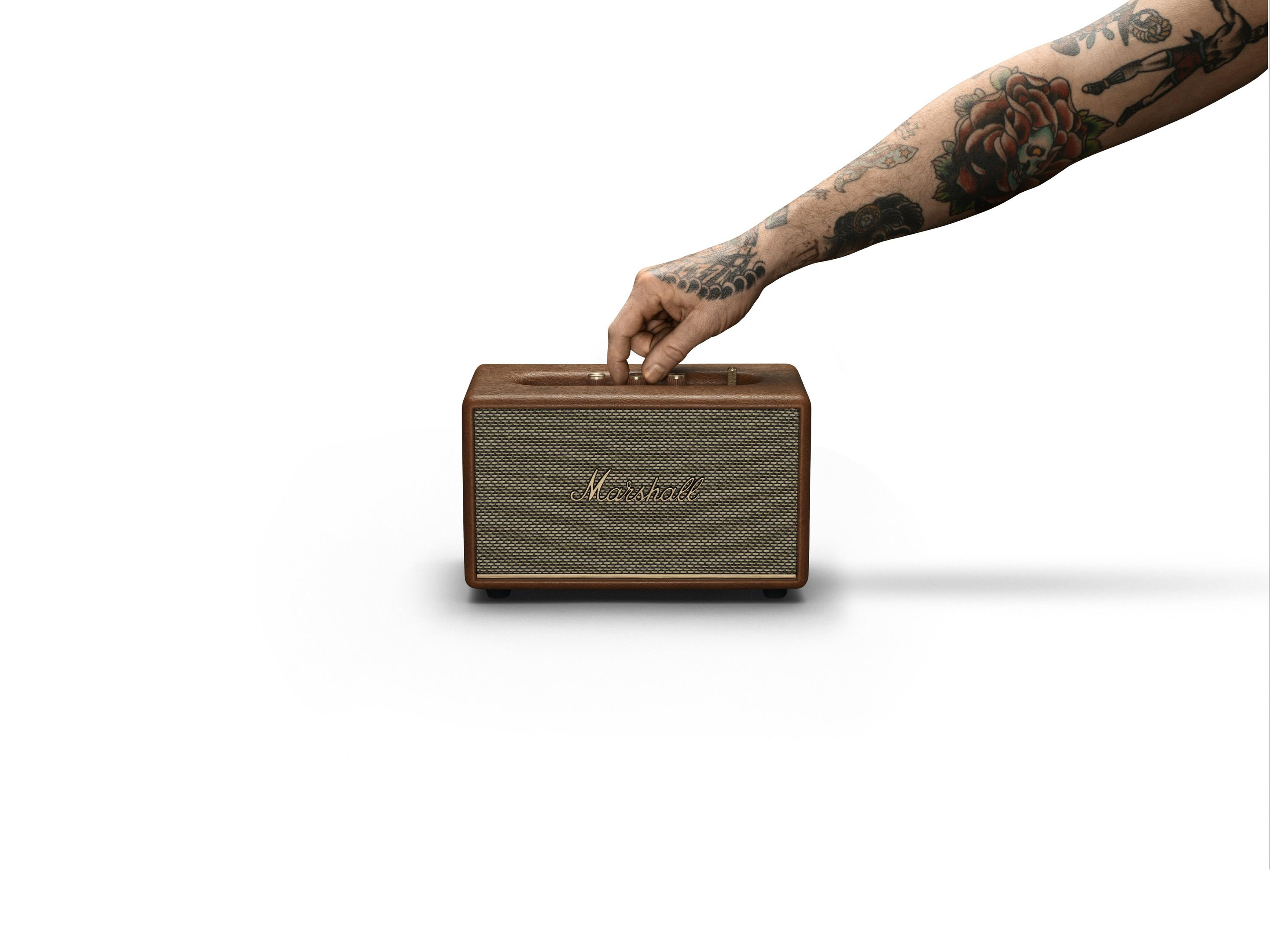 La mano de una persona sosteniendo un altavoz marrón con el logo de Marshall.