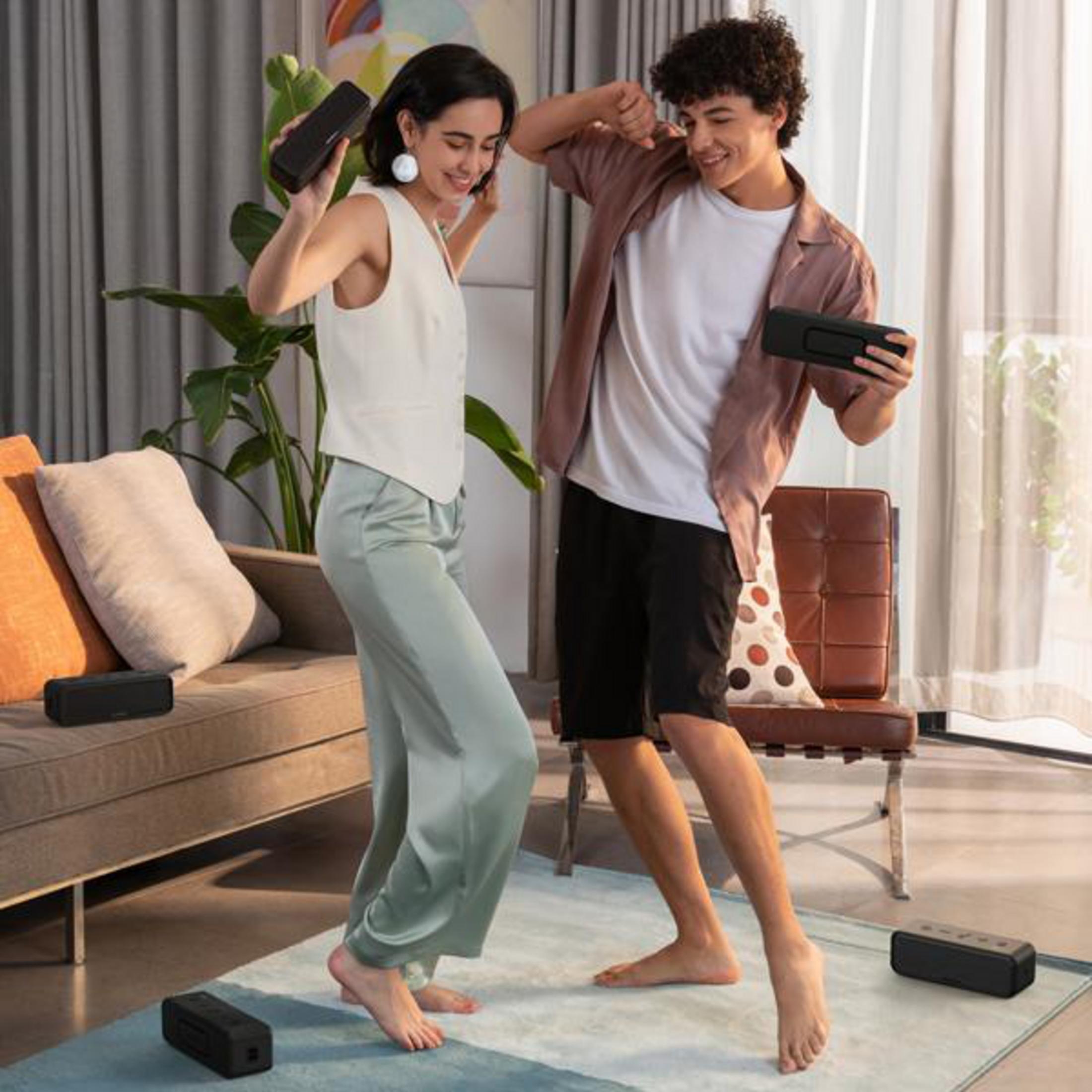 Para tańczy z głośnikami w dłoniach. Kilka głośników na podłodze. Neutralne kolory.
