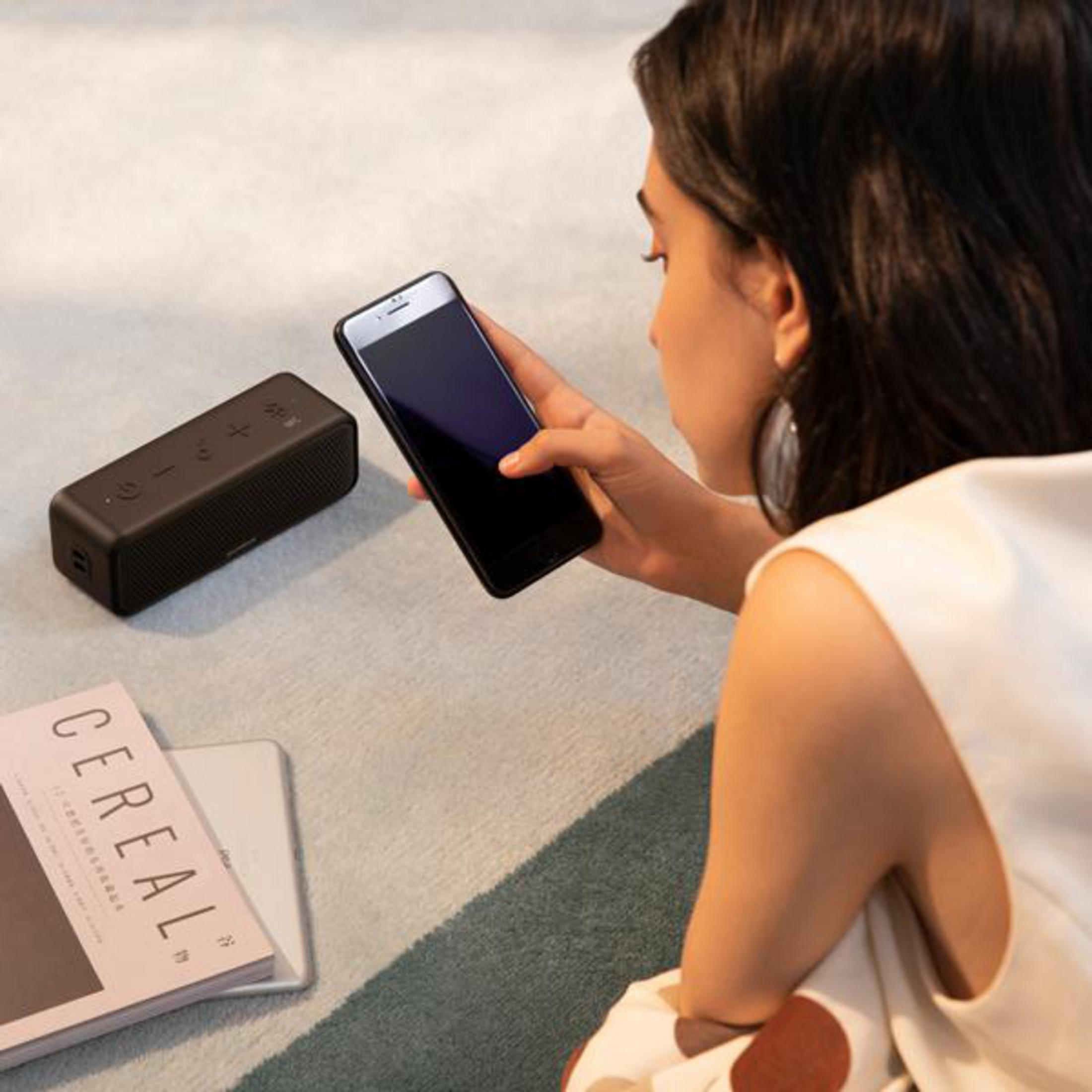 Kobieta używa telefonu, czarnego głośnika i magazynu na dywanie.