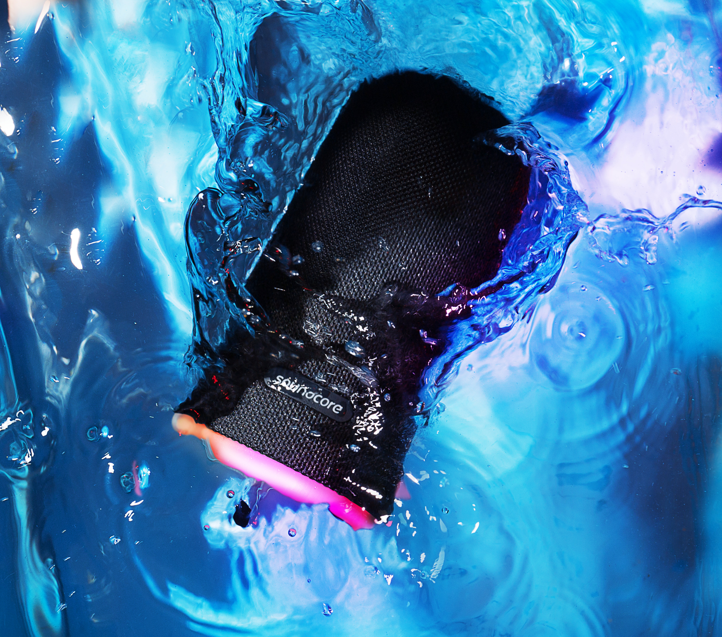 Czarny głośnik Soundcore zanurzony w niebieskiej wodzie z rozpryskami i odbiciami.