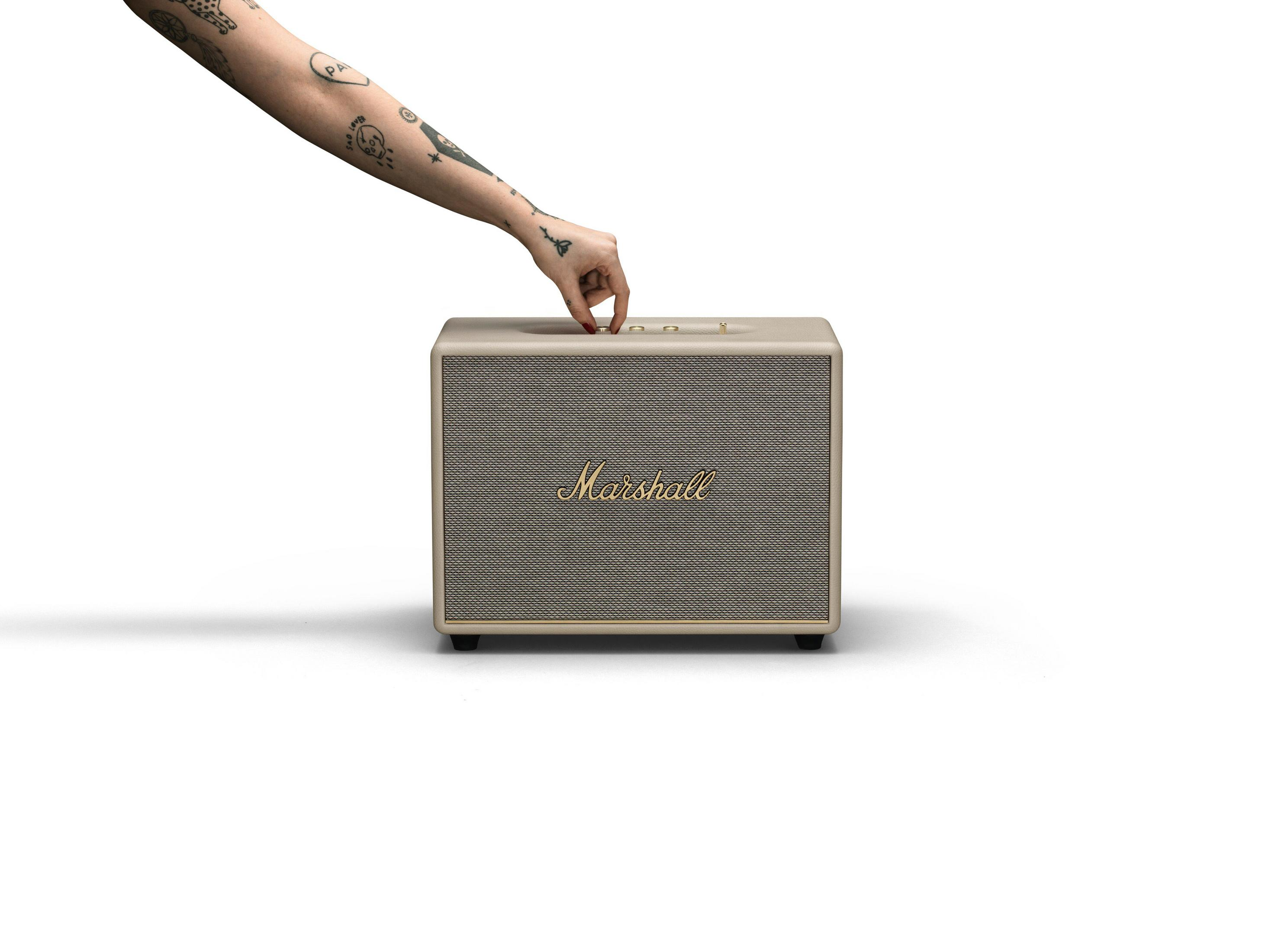 Hand dreht Knopf an Marshall-Lautsprecher, auf weißem Hintergrund. Marshall-Logo sichtbar.