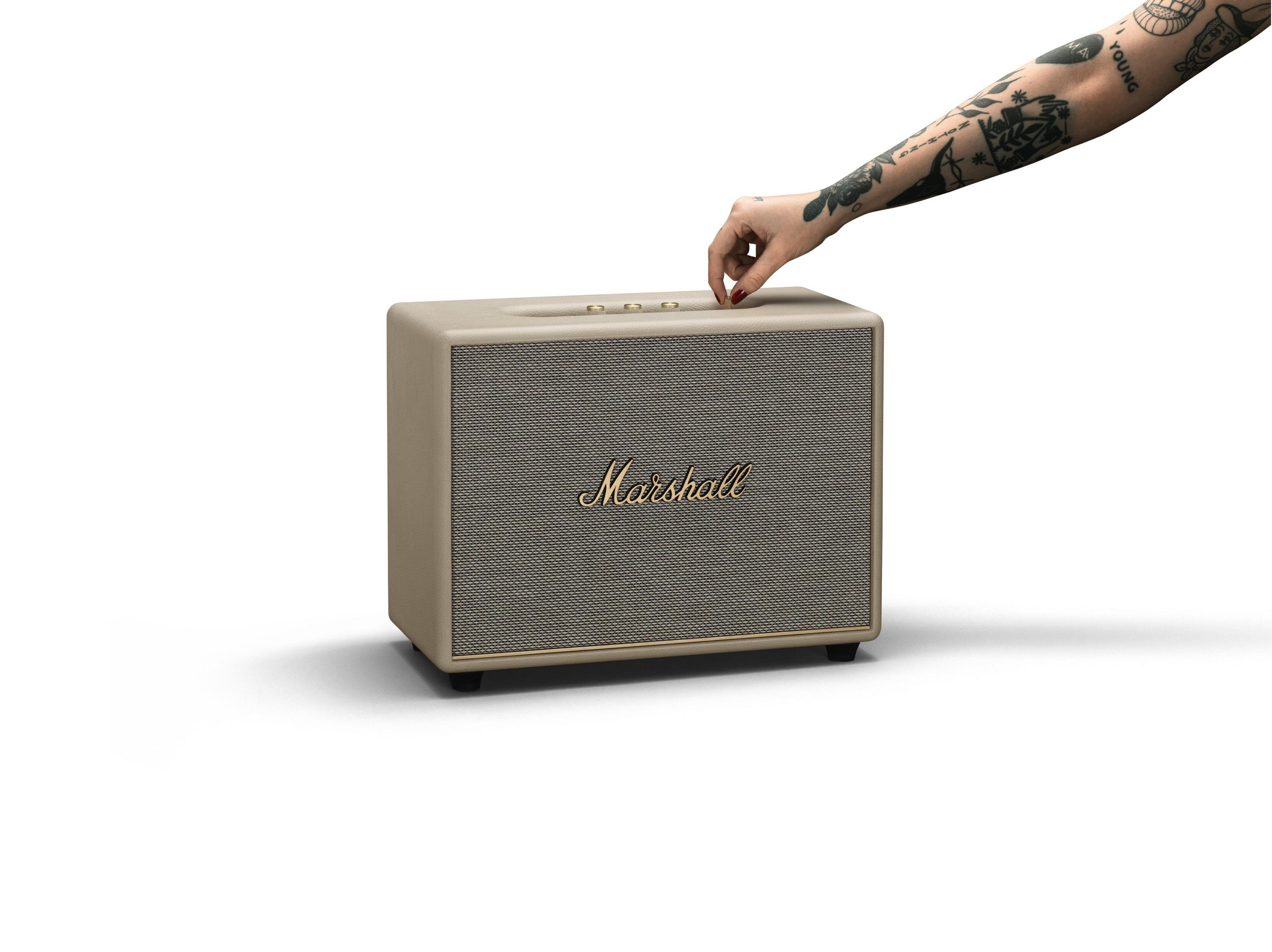 Eine Hand dreht einen Knopf an einem Marshall-Lautsprecher. Der Lautsprecher ist beige.