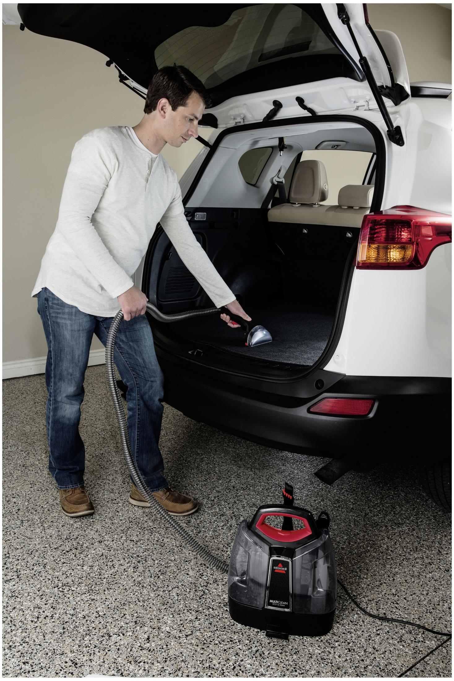 Un uomo aspira l'interno di un SUV bianco con un pulitore per tappeti portatile Bissell.