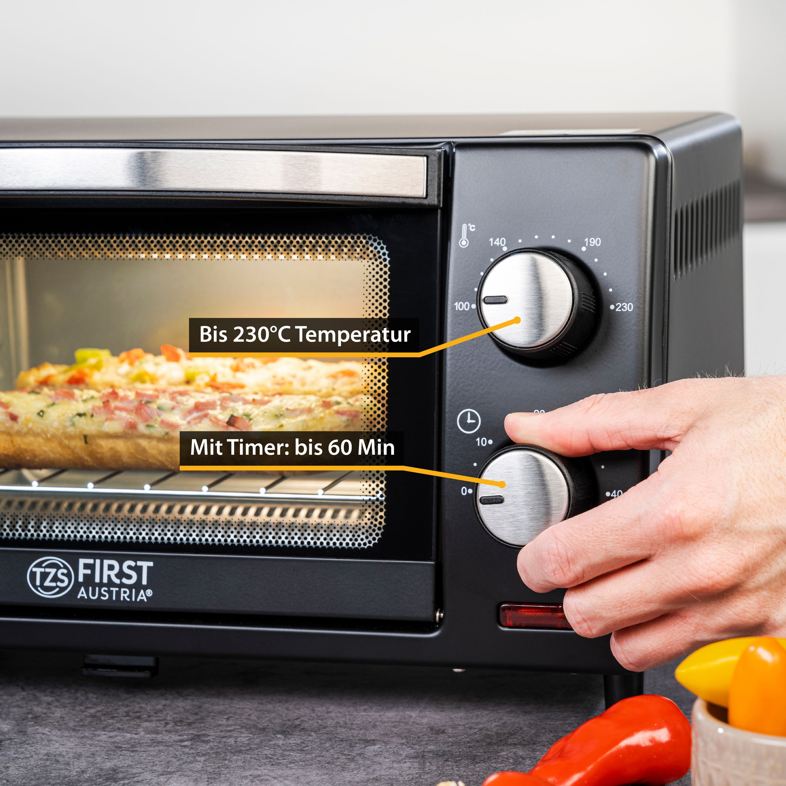Mini forno nero con comandi, pizza all'interno e una mano che regola una manopola.