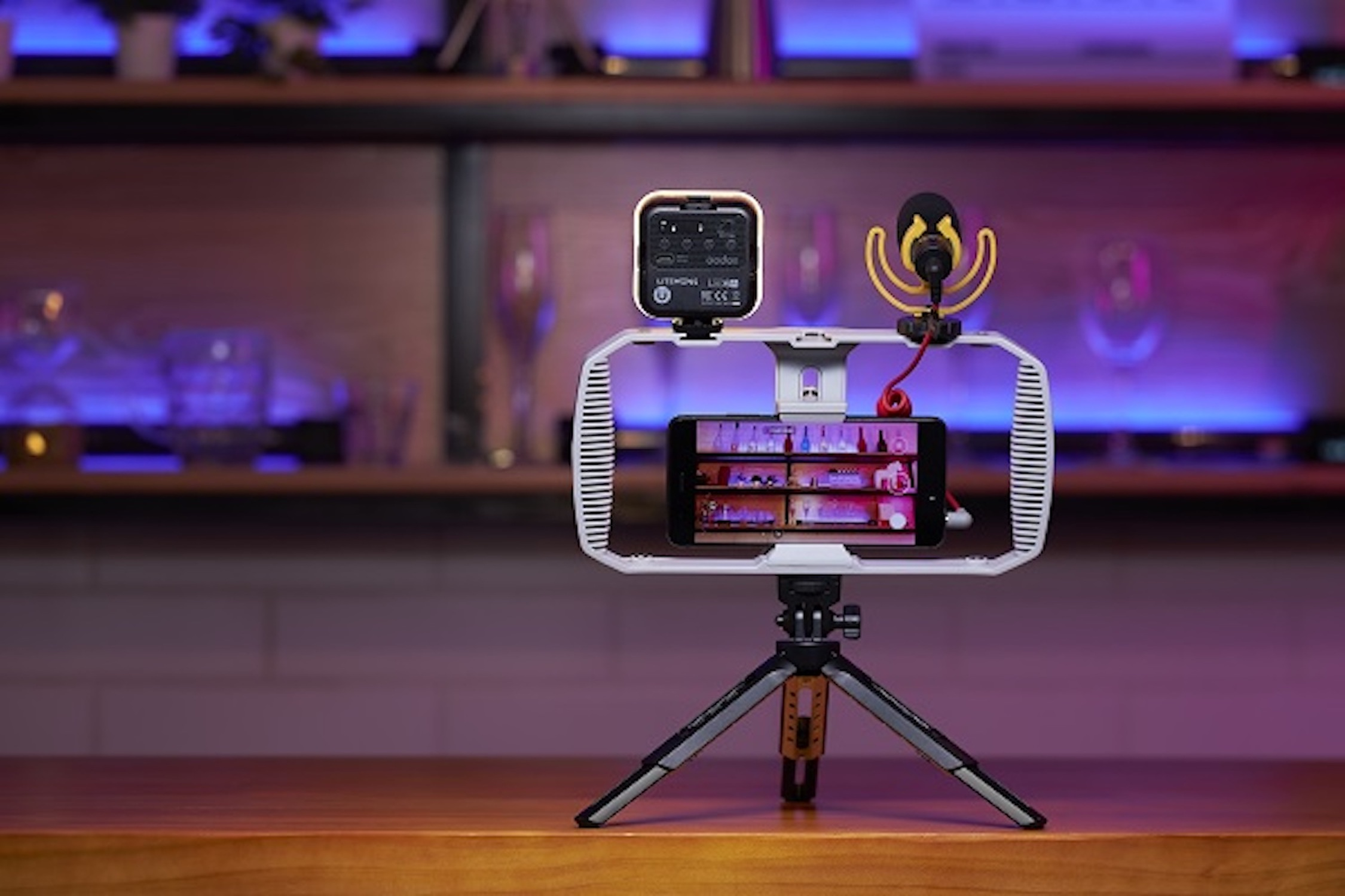 Ein Smartphone, Mikrofon und Licht auf einem Stativ, auf einer Holzoberfläche, vor einer Bar.