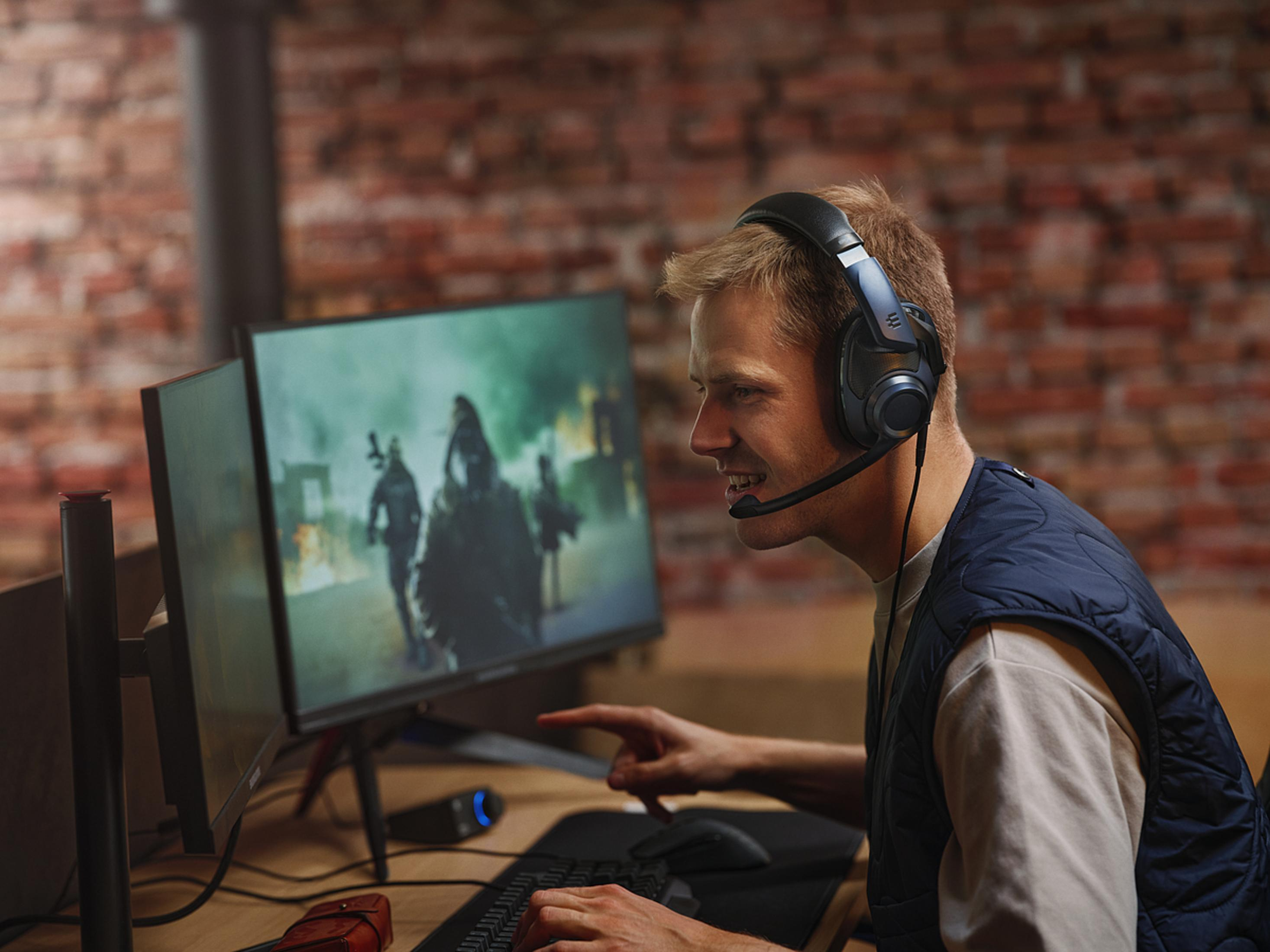 Mężczyzna z zestawem słuchawkowym gra, patrząc na monitor z sceną walki.
