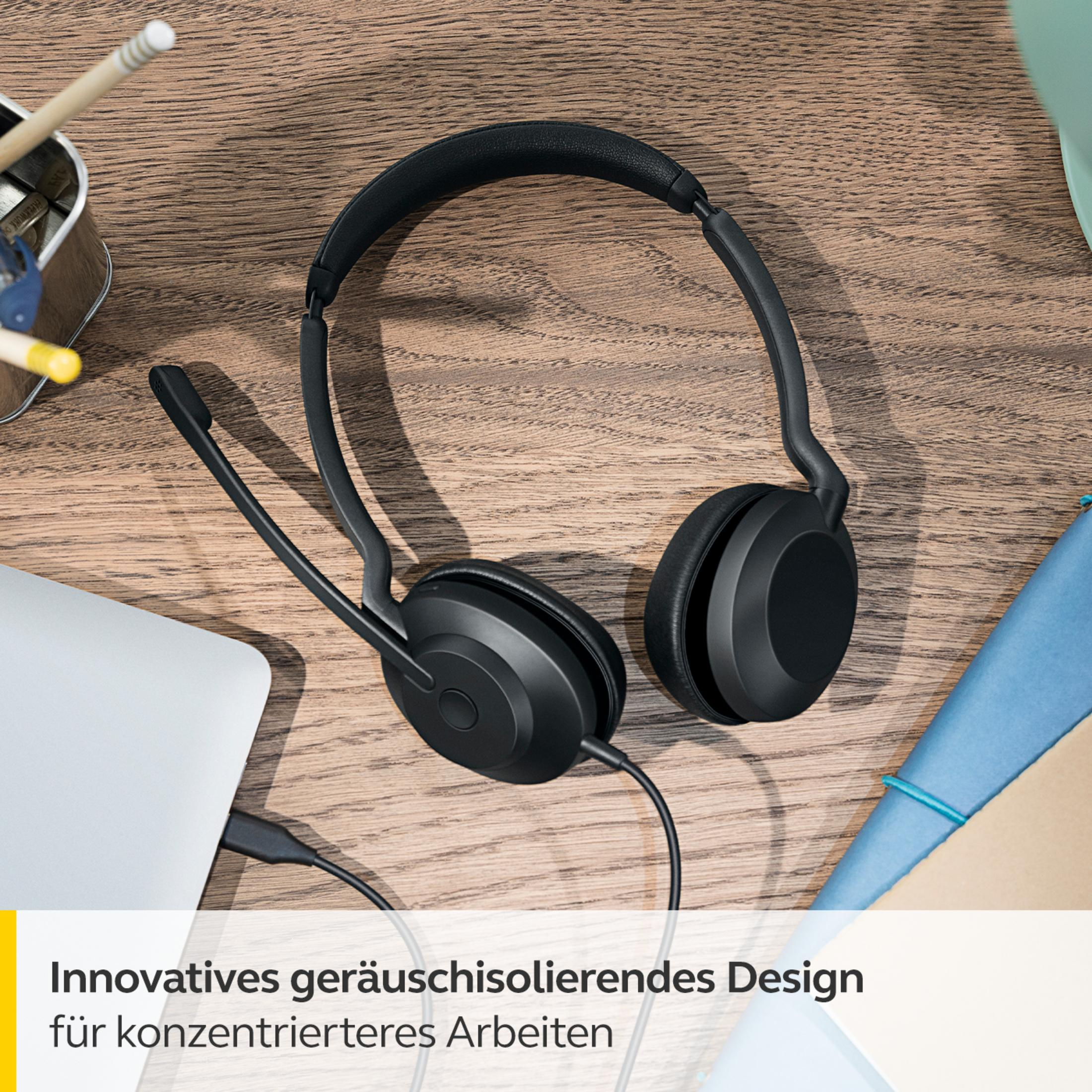 Schwarzes Headset mit Mikrofon auf einem Holztisch. Es gibt einen Laptop und etwas Bürobedarf.