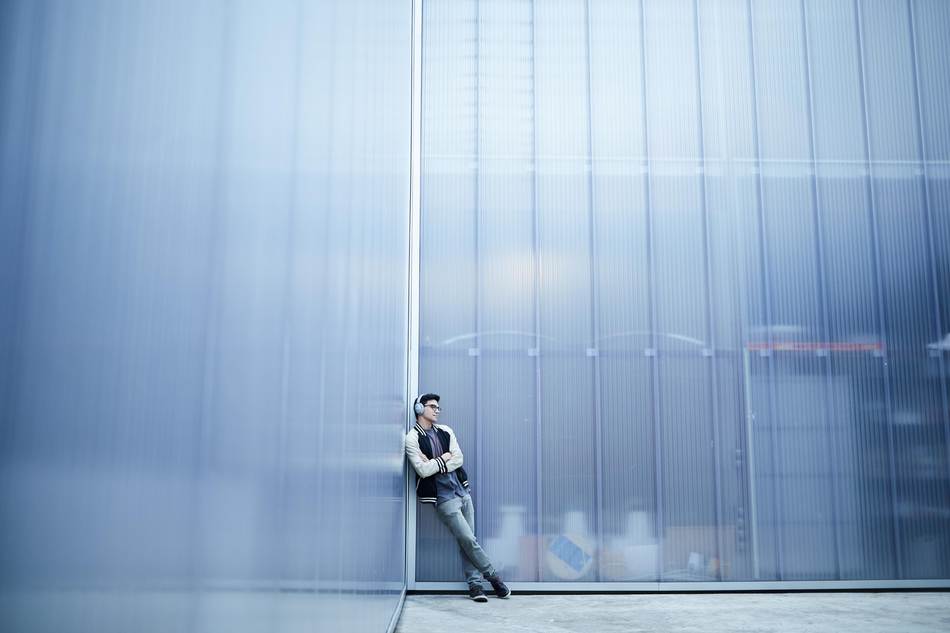 Eine Person mit Kopfhörern lehnt an einer transparenten blauen Wand.