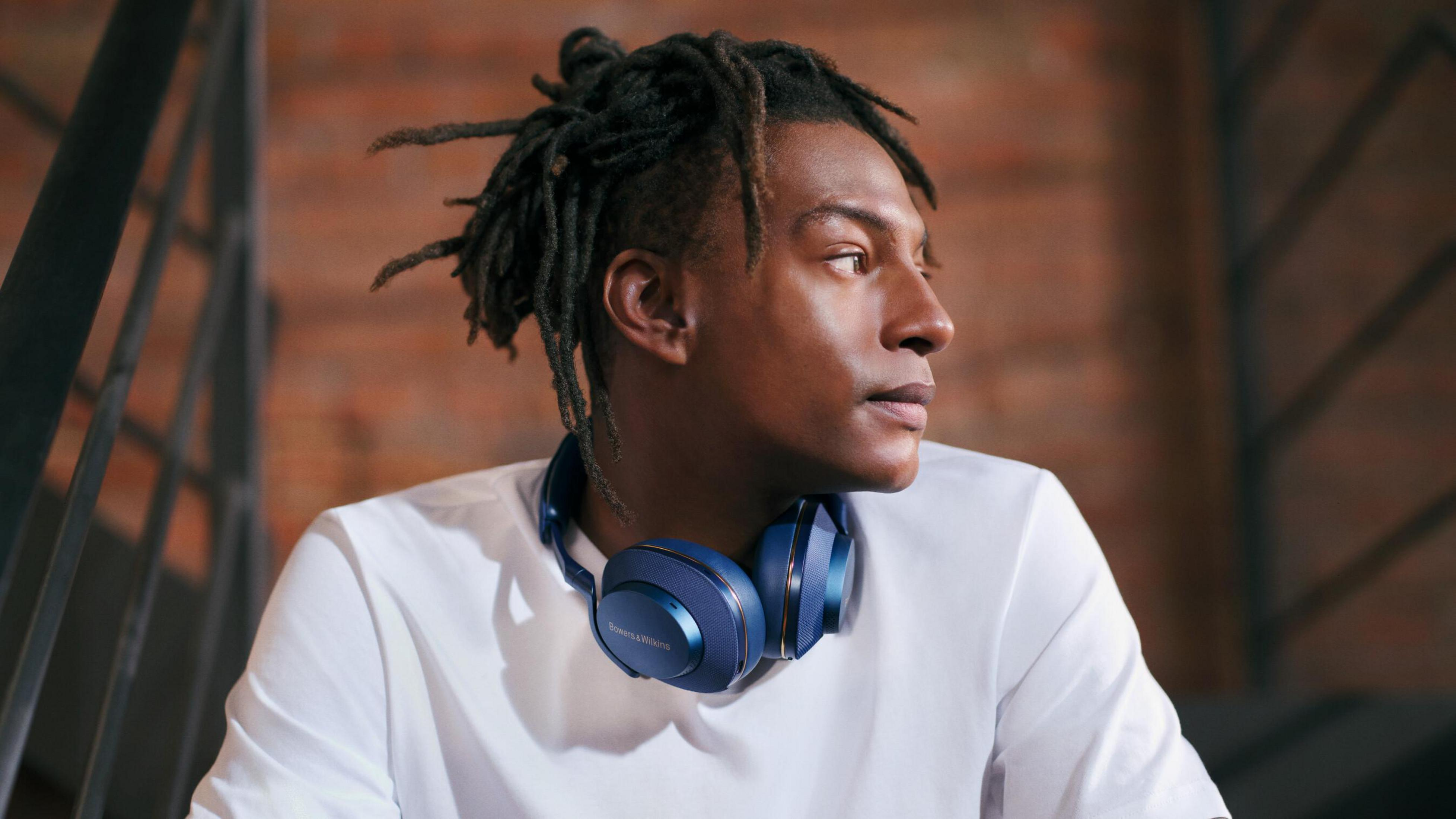Ein Mann mit Dreadlocks trägt blaue Kopfhörer und sitzt auf einer Treppe. Im Hintergrund eine Ziegelmauer.