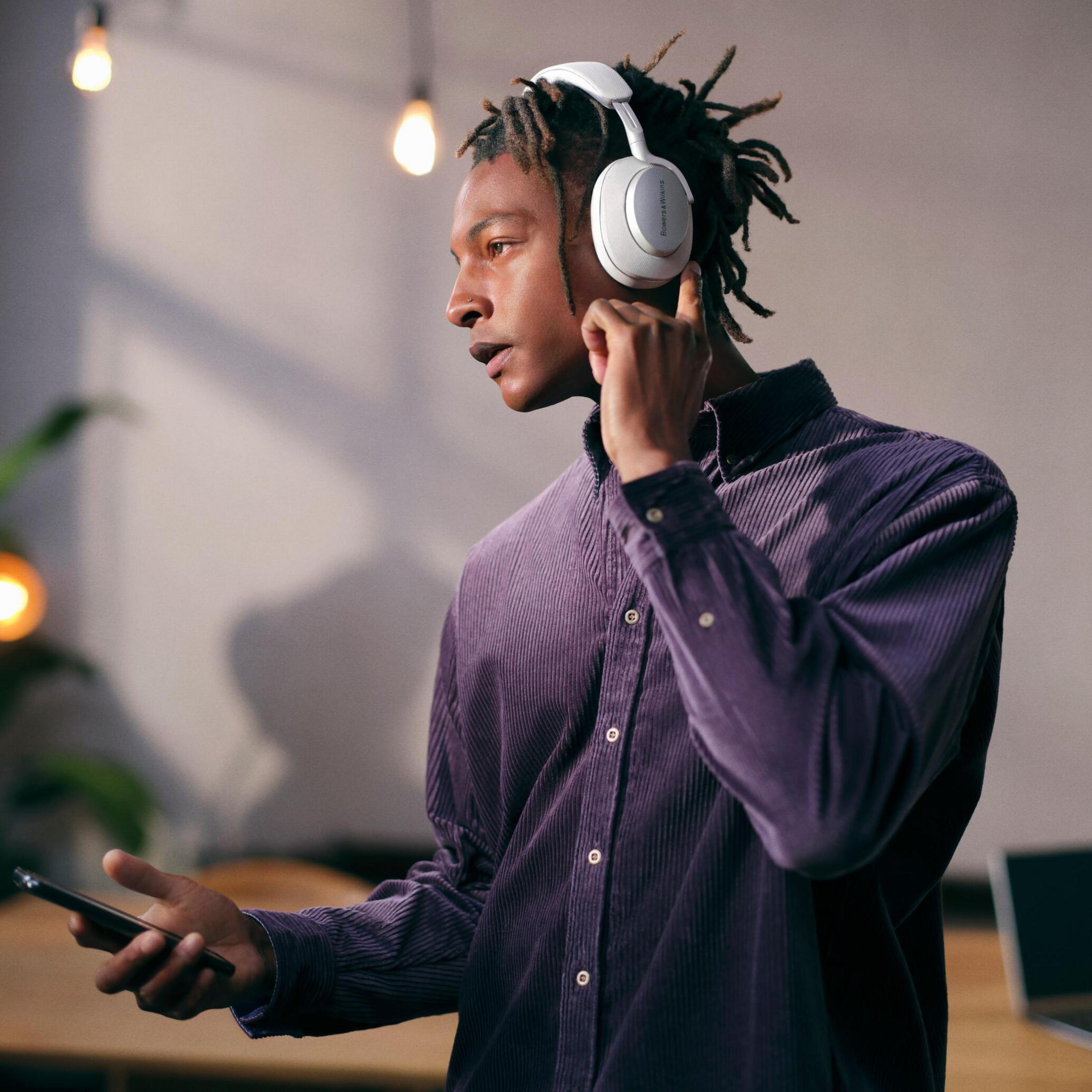 Mężczyzna w białych słuchawkach patrzy w lewo. Trzyma telefon i ma na sobie fioletową koszulę.