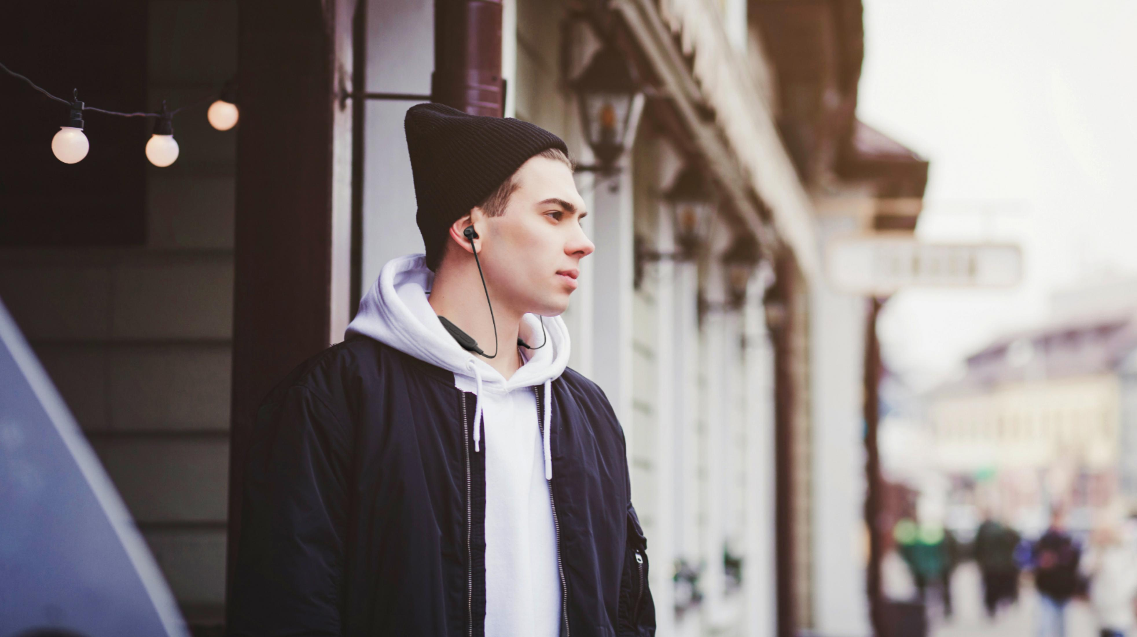 Mężczyzna w czarnej czapce i czarnej kurtce słucha muzyki w słuchawkach.