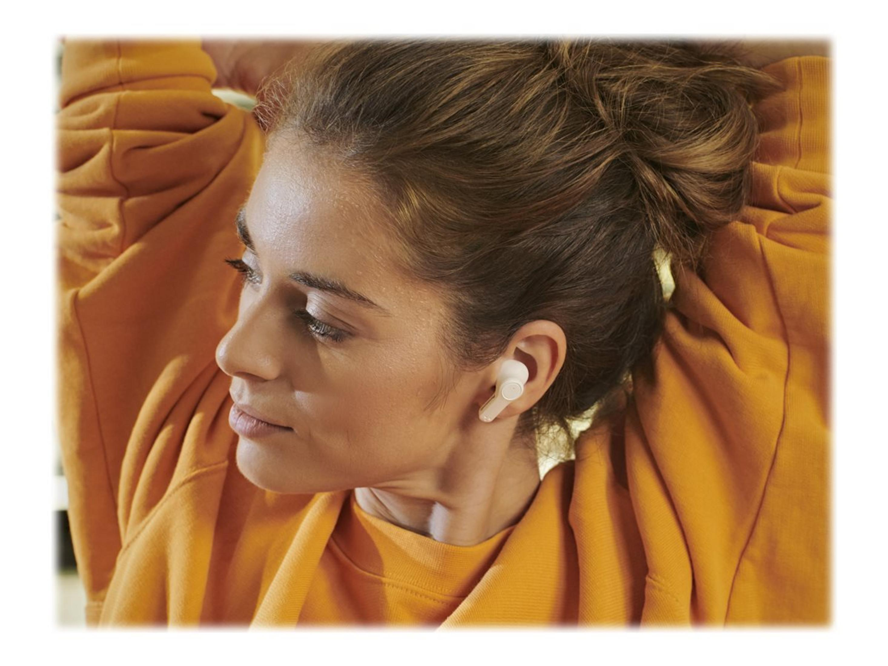 Kobieta w białych słuchawkach, patrząca w lewo, w pomarańczowym swetrze.